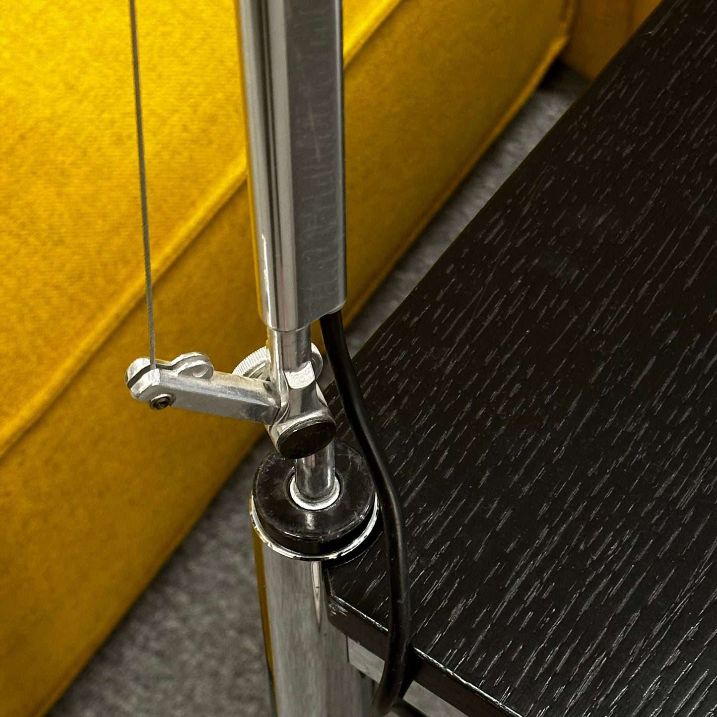 Close-up of silver Artemide Tolomeo Tavolo halogen lamp clamp mounted on black wood table edge near yellow sofa