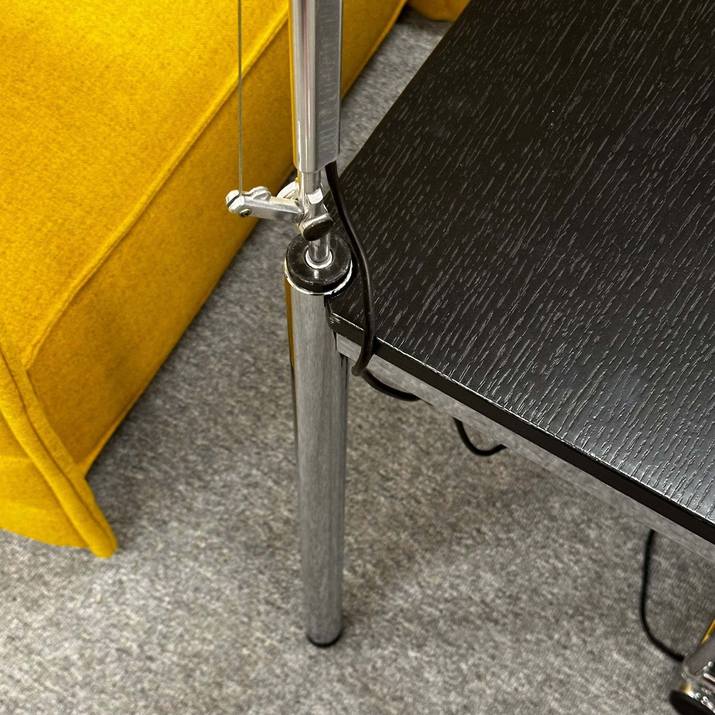 Close-up of Artemide Tolomeo Tavolo silver lamp mount attached to black table near yellow chair on gray carpet