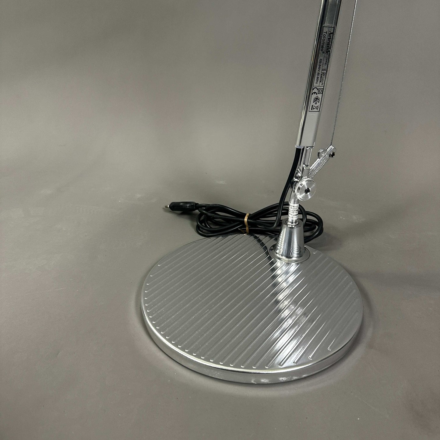 Polished aluminum base of Artemide Tolomeo Tavolo desk lamp with adjustable arm and power cord.