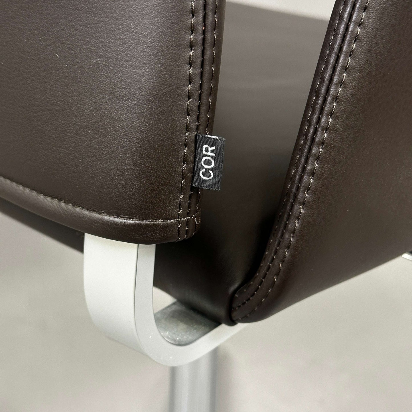 Nahaufnahme des COR Fino Drehstuhls mit dunkelbraunem Leder und poliertem Aluminiumgestell