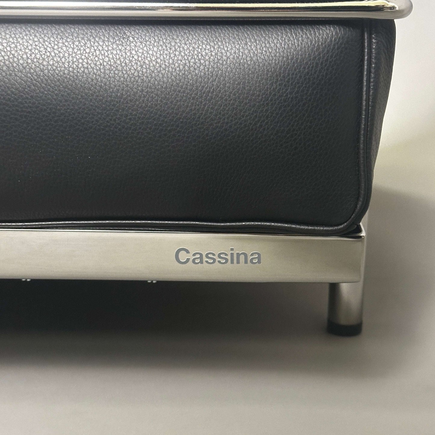 Close-up of Cassina LC2 black leather chair corner with chrome steel frame and Cassina logo engraving