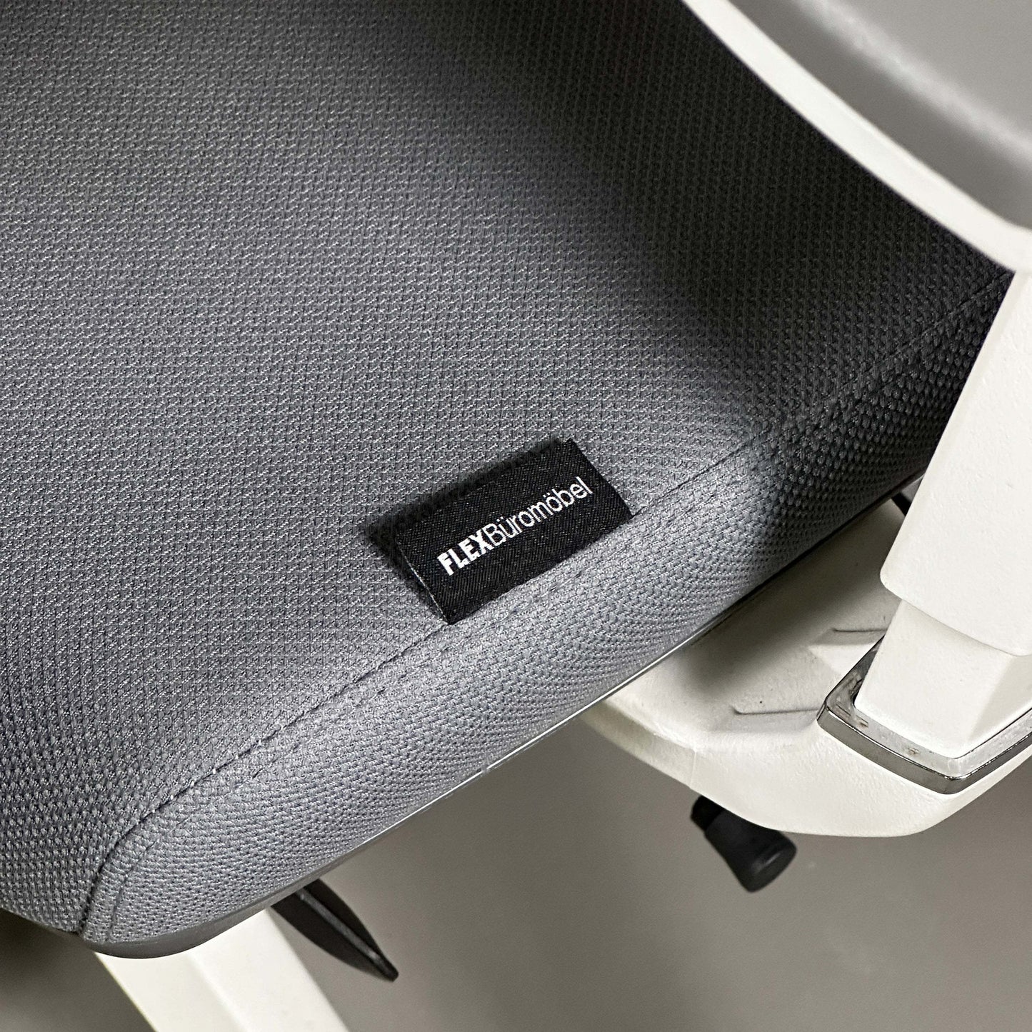 Close-up of ergonomic Bürostuhl seat with grey fabric and white aluminum frame showing FLEXBüromöbel label