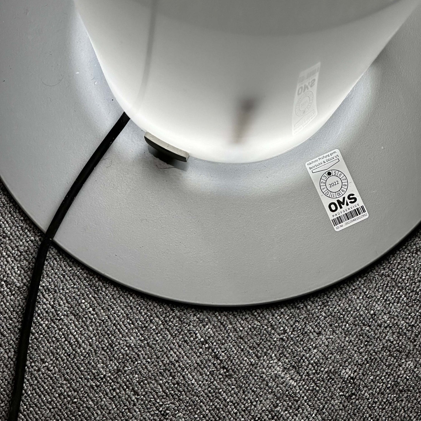 Base of the FLOS Stylos Stehlampe floor lamp on grey carpet with power cord and certification label