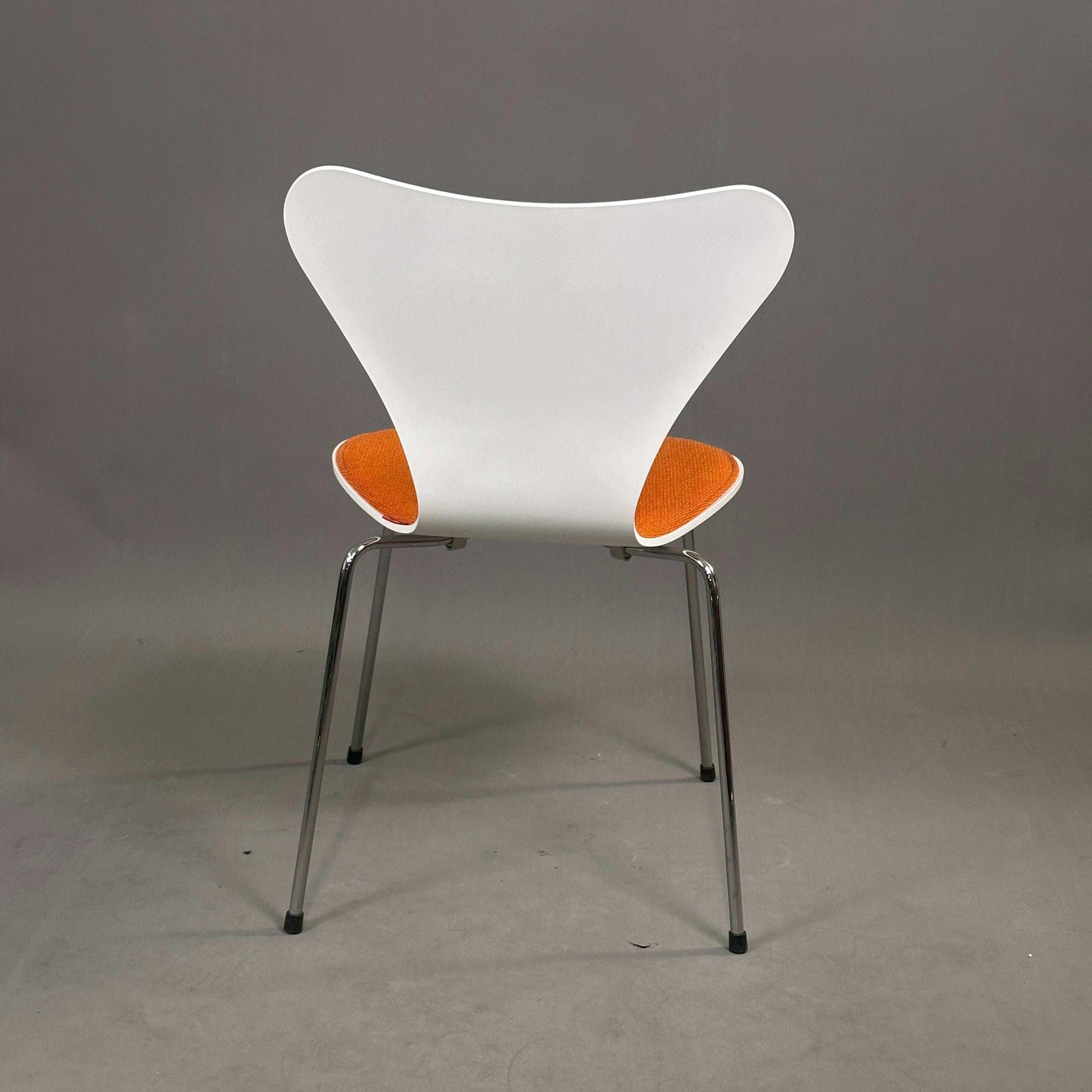 Fritz Hansen Serie 7 Stapelstuhl mit weißer Holzsitzschale, orangefarbener Polsterung und Chromgestell.