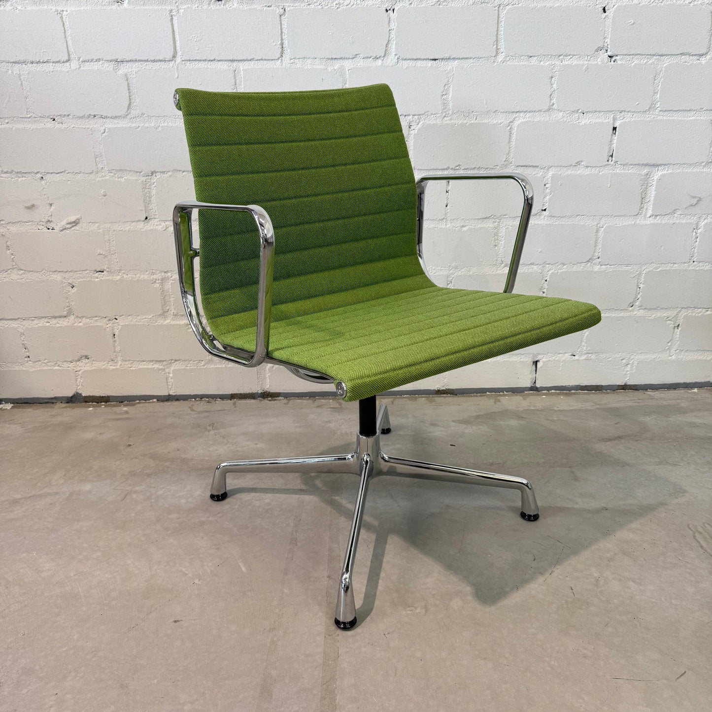 Vitra EA 108 Hopsak swivel chair in green fabric with chrome frame against white brick wall