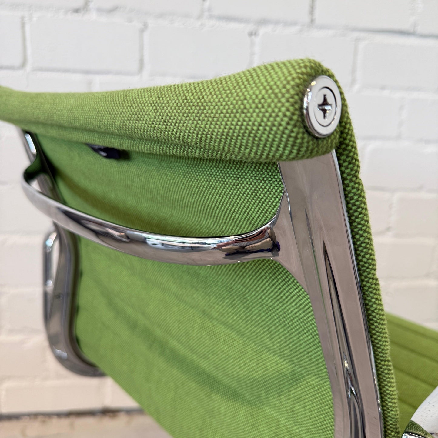 Close-up of Vitra EA 108 Hopsak office chair in green wiesengrün fabric with chrome frame against white brick wall