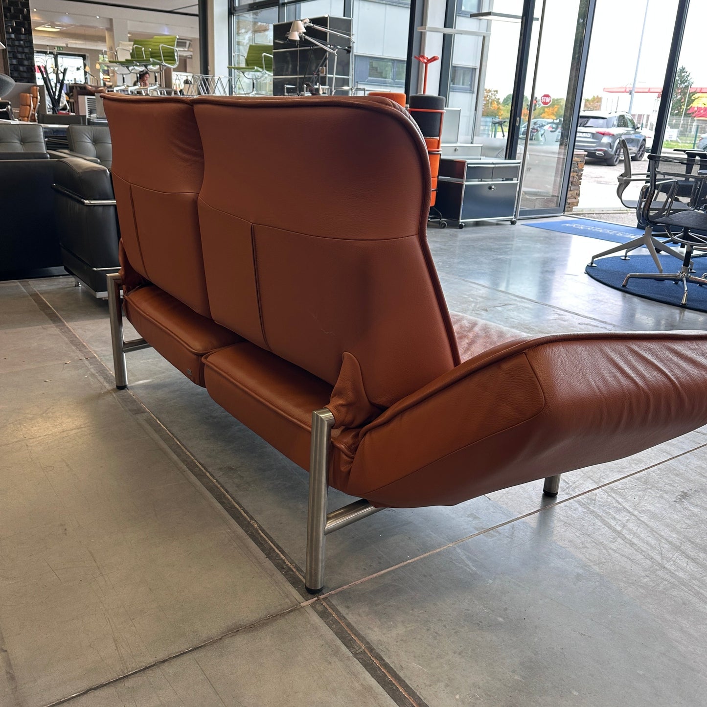 De Sede Drehsofa DS450 Twist aus nougatfarbenem Leder mit drehbaren Sitzelementen und kippbaren Rückenlehnen in modernem Showroom