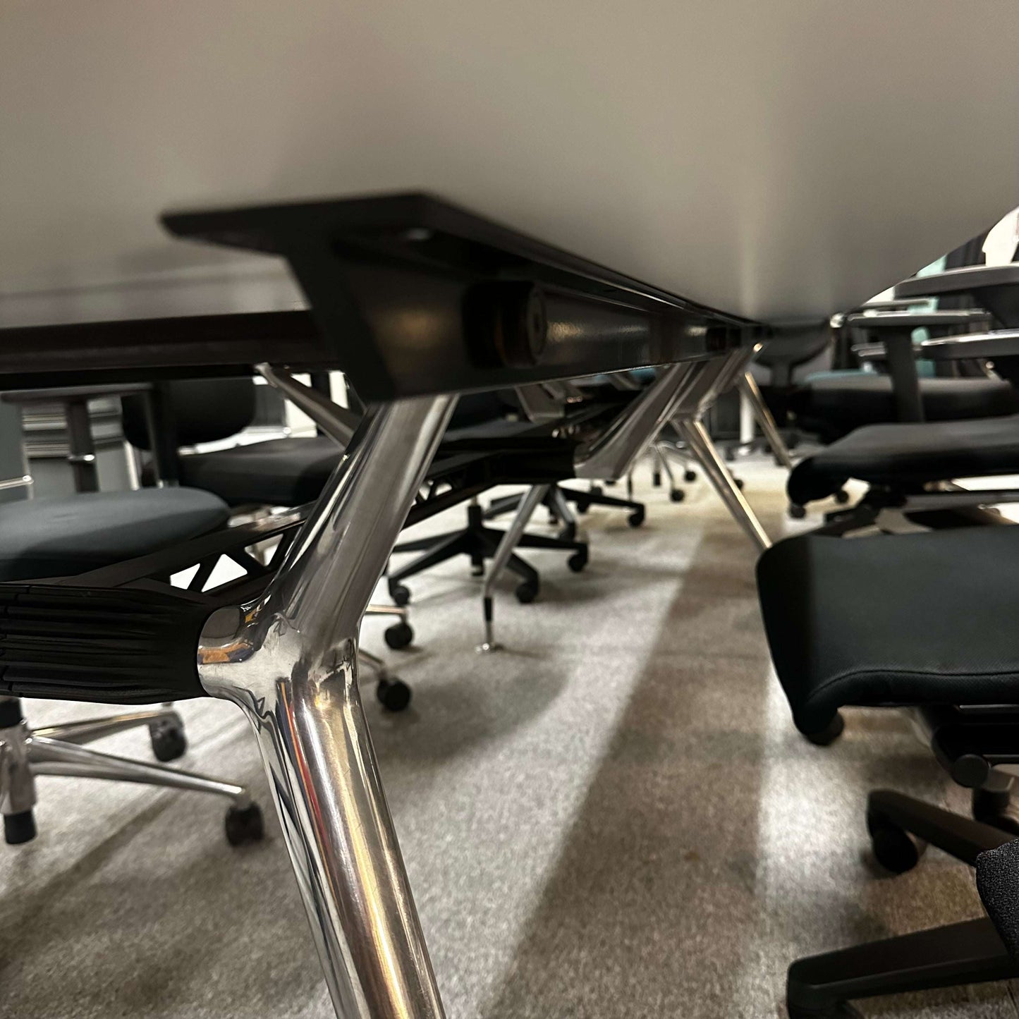 4 meter long white and silver conference table with metal legs surrounded by black office chairs
