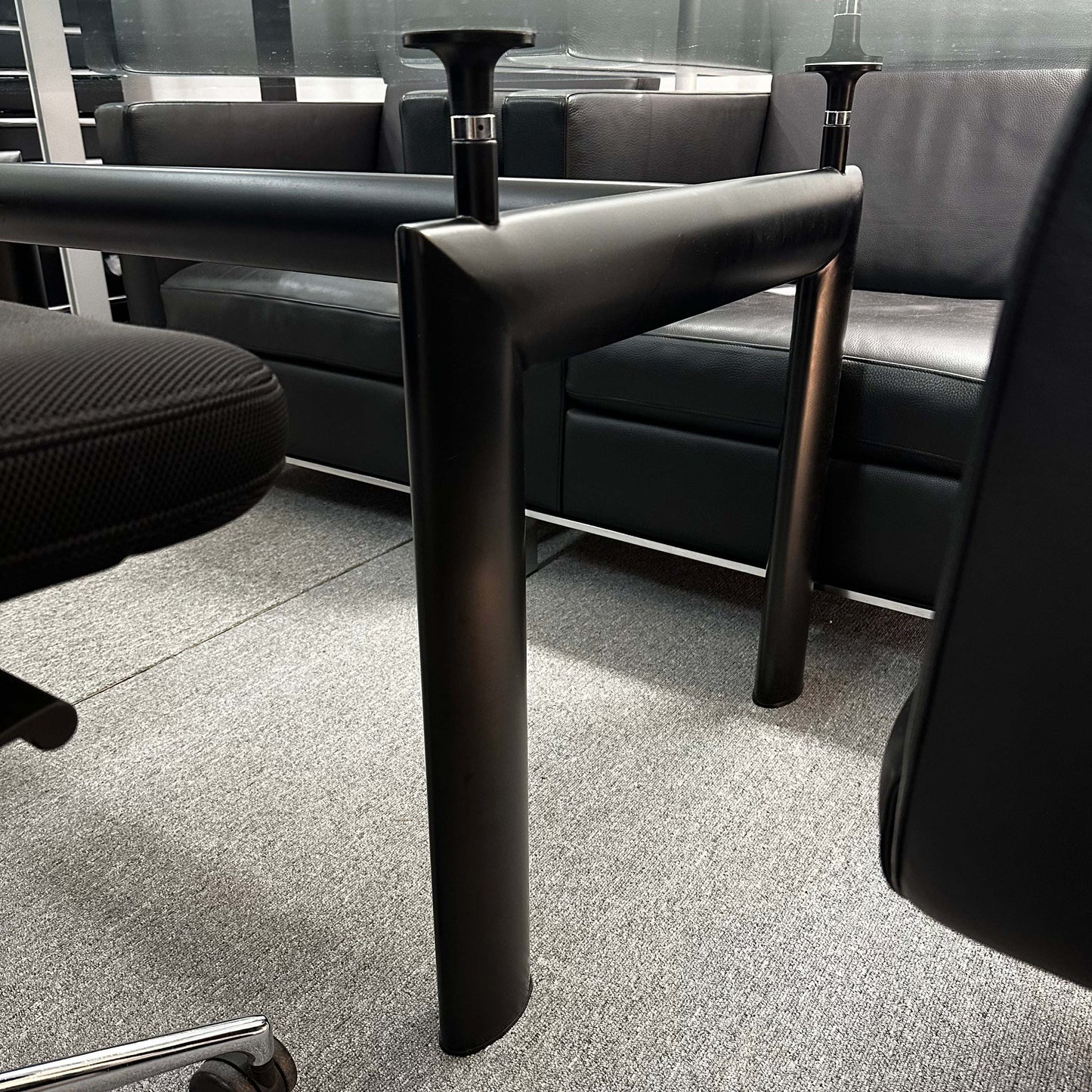 Black adjustable table legs of LC6 Tisch replica with glass tabletop in office setting