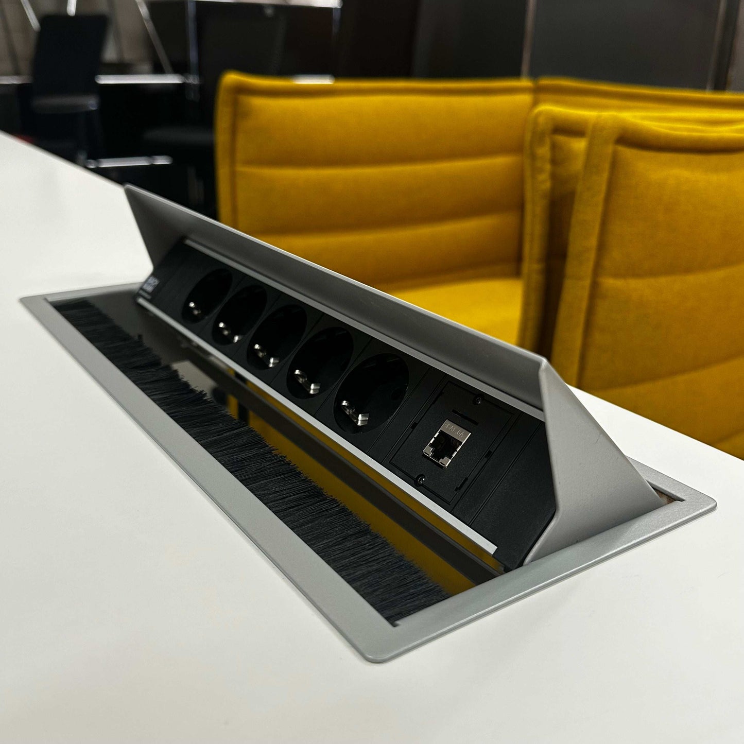 Lampert Eiermann Tisch with built-in power outlets and network port on white tabletop and yellow office chairs in background