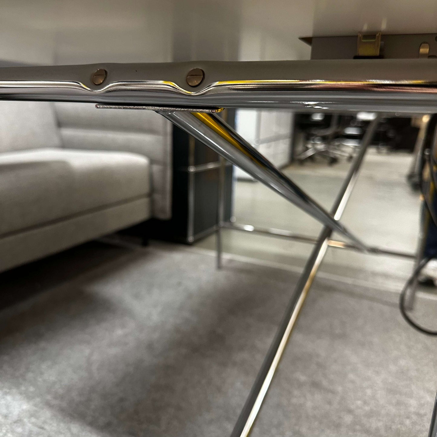 Close-up of the chrome crossed side frame of the Lampert Eiermann Tisch with a white tabletop in a modern room setting