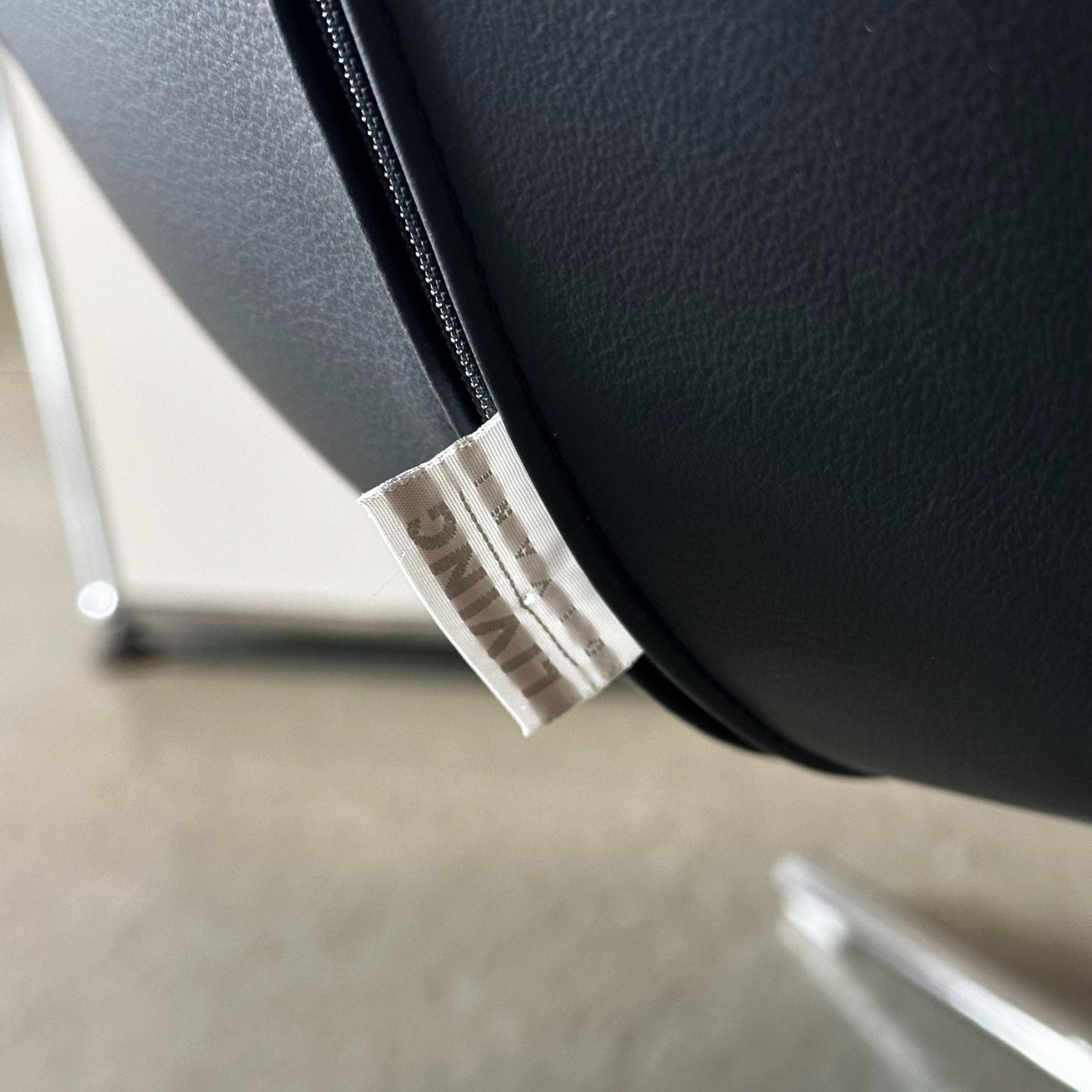 Close-up of black Living Divani Ledersessel Jelly leather armchair with tag and sleek metal legs.