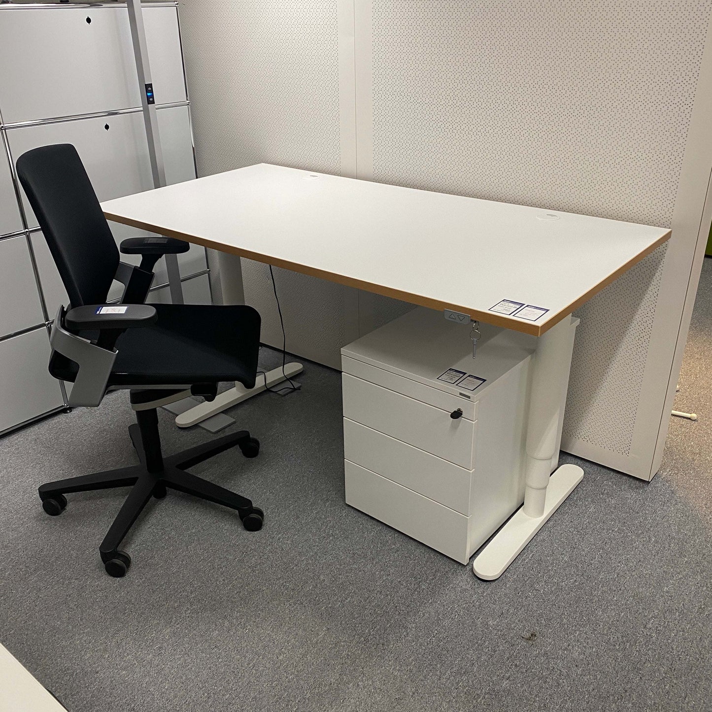 White 160x80cm electrically height-adjustable desk with multiplex edge, cable management, and black office chair in modern office setup