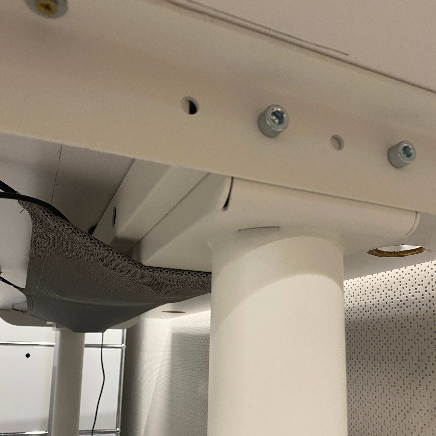 Close-up of the underside of a white electrically height-adjustable desk with cable management net and white legs, Schreibtisch 160x80cm model Bekant by Ikea