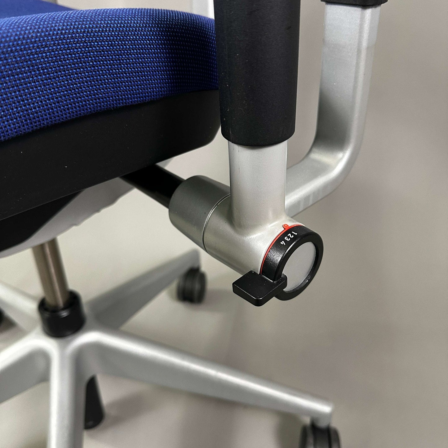 Close-up of adjustment knob on blue Steelcase Please ergonomic office chair with silver metal frame and caster wheels