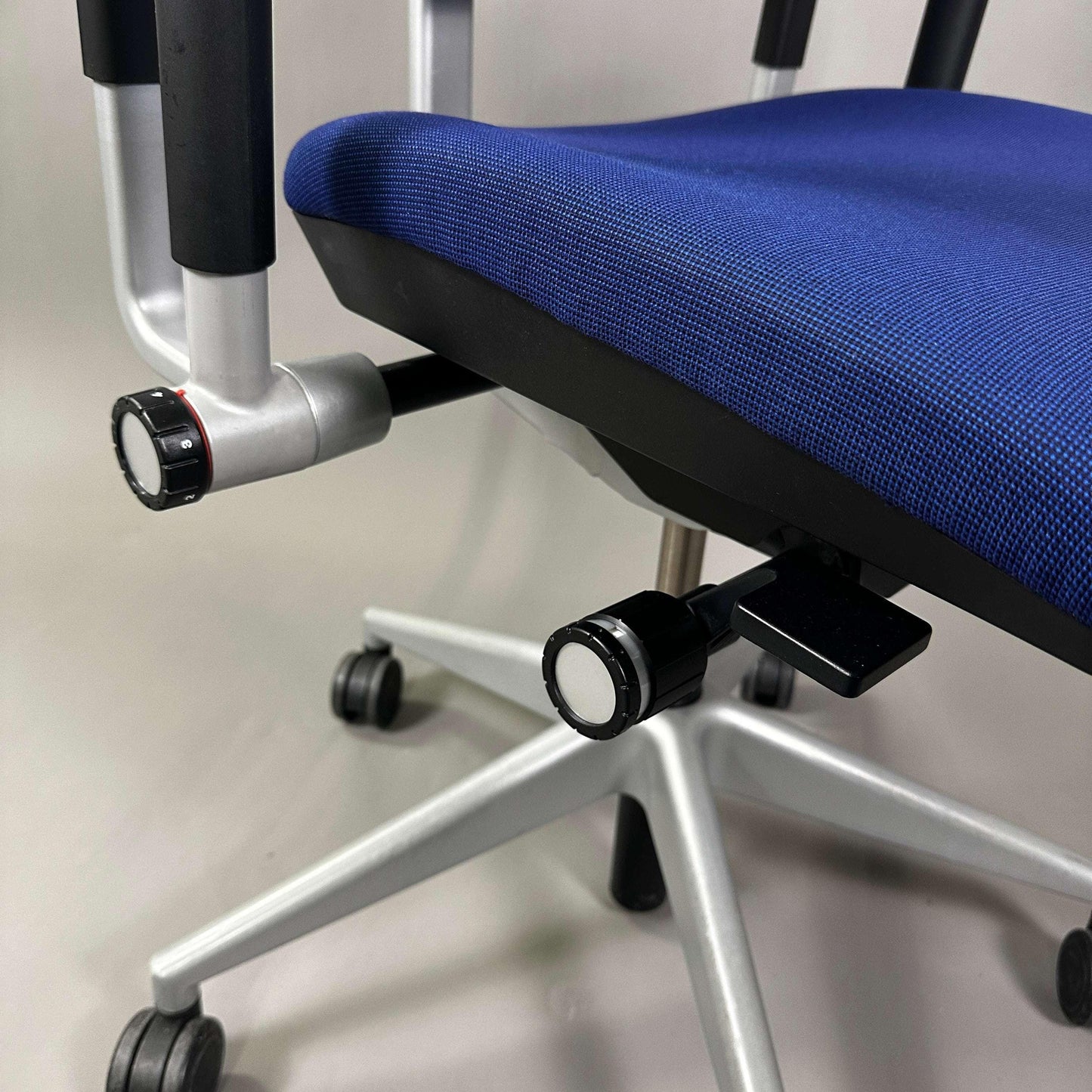 Close-up of the blue Steelcase Please office chair seat with adjustable knobs and silver metal base on casters