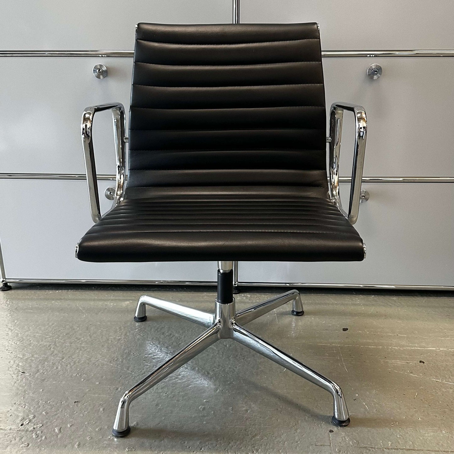 Black faux leather office chair in Vitra EA108 design replica with chrome armrests and base