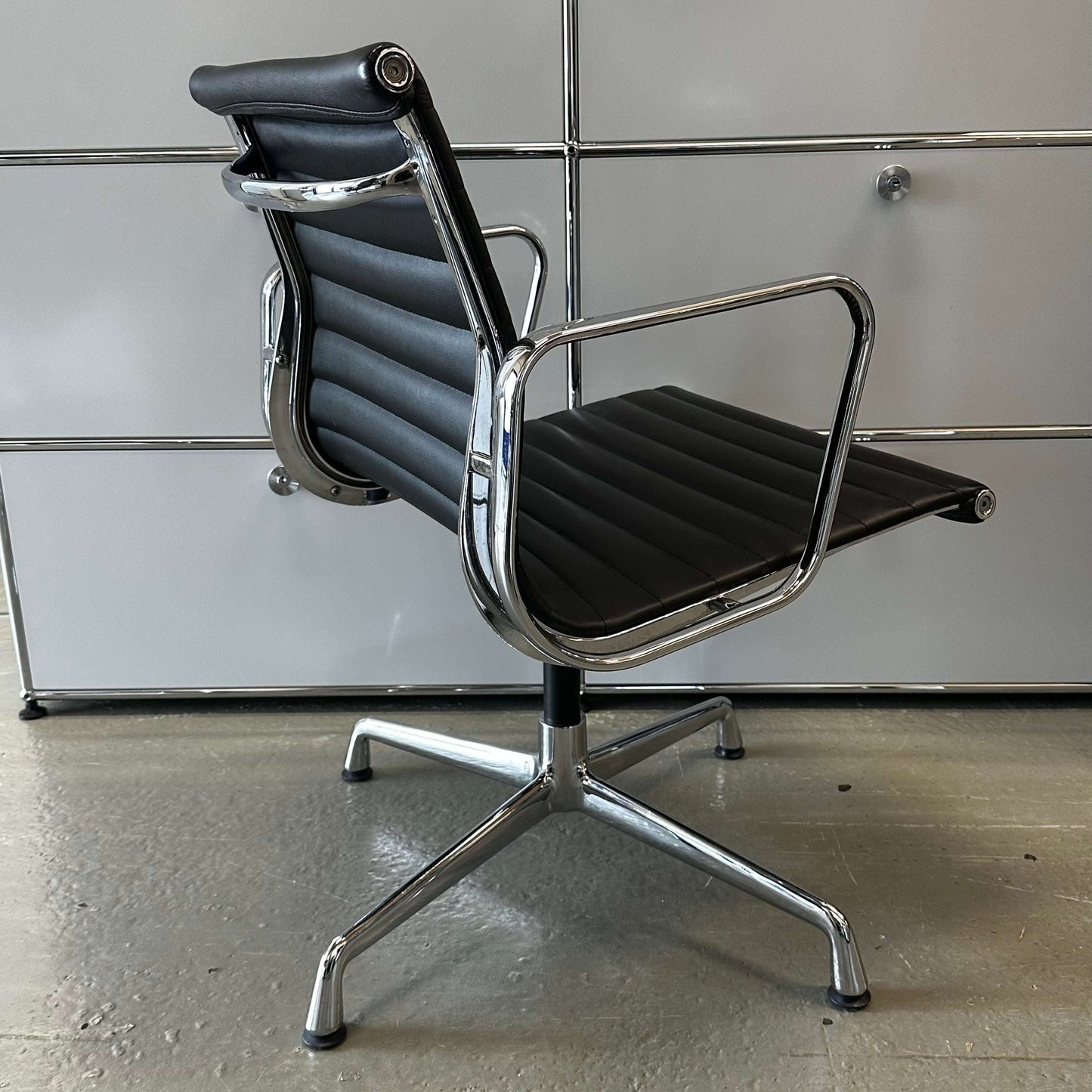Black Vitra EA108 style office chair replica with chrome frame and leatherette upholstery
