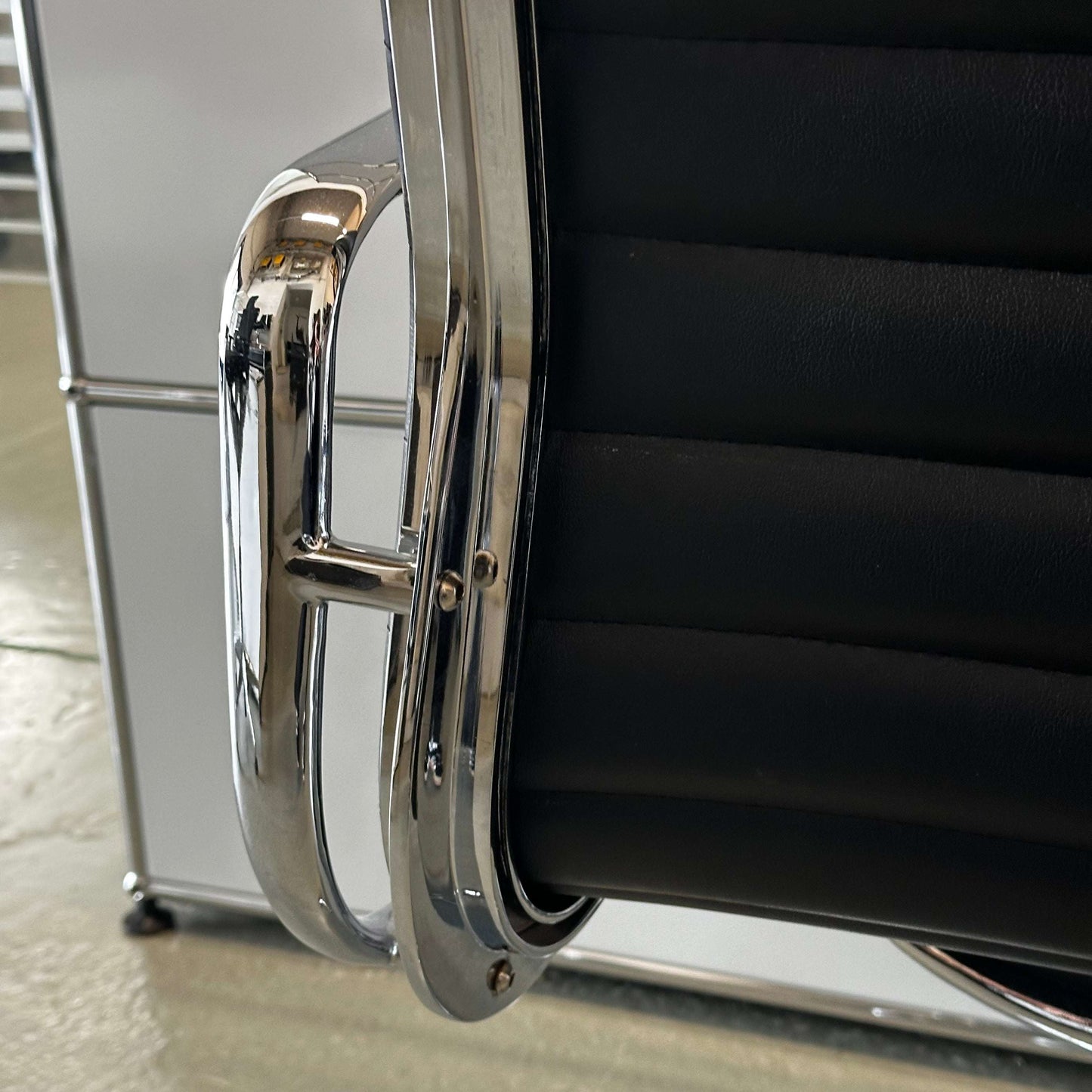 Close-up of black faux leather Stuhl im Vitra EA108 replica with chrome armrest detail