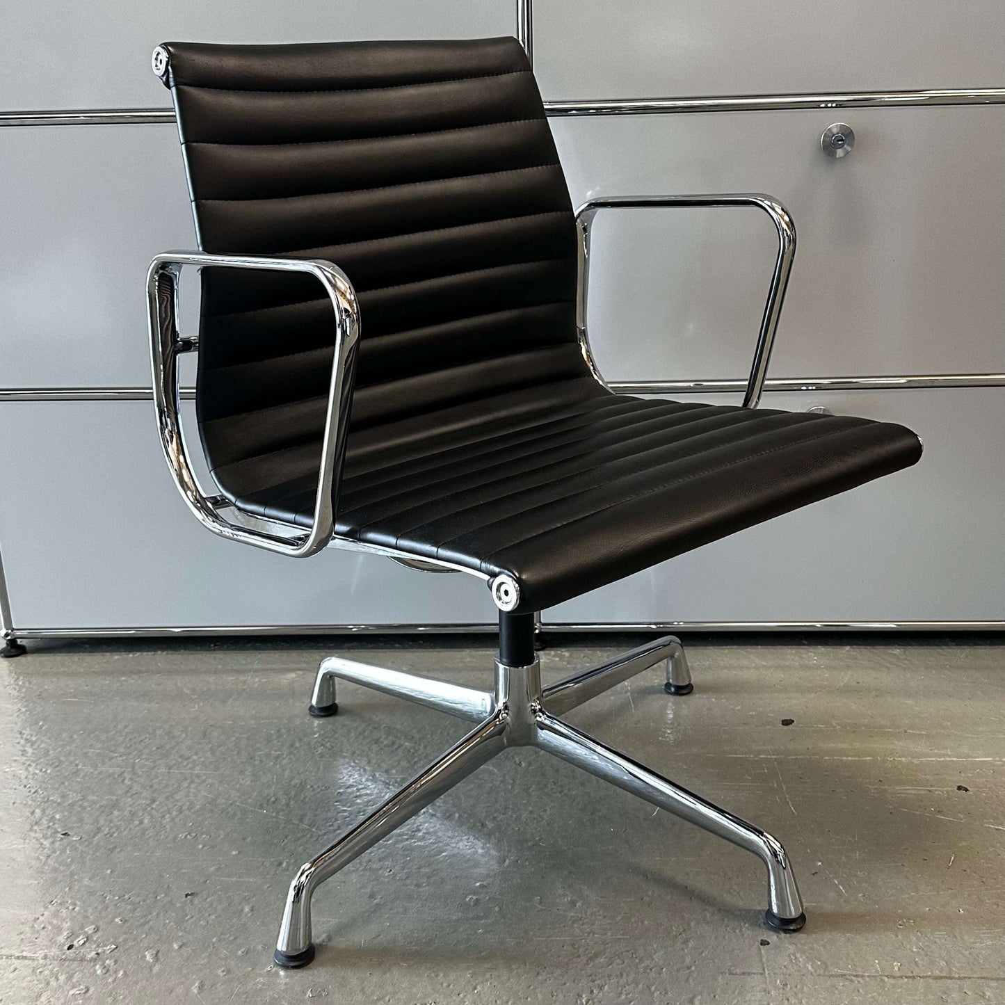Black Vitra EA108 style office chair replica with chrome frame and faux leather seat and backrest