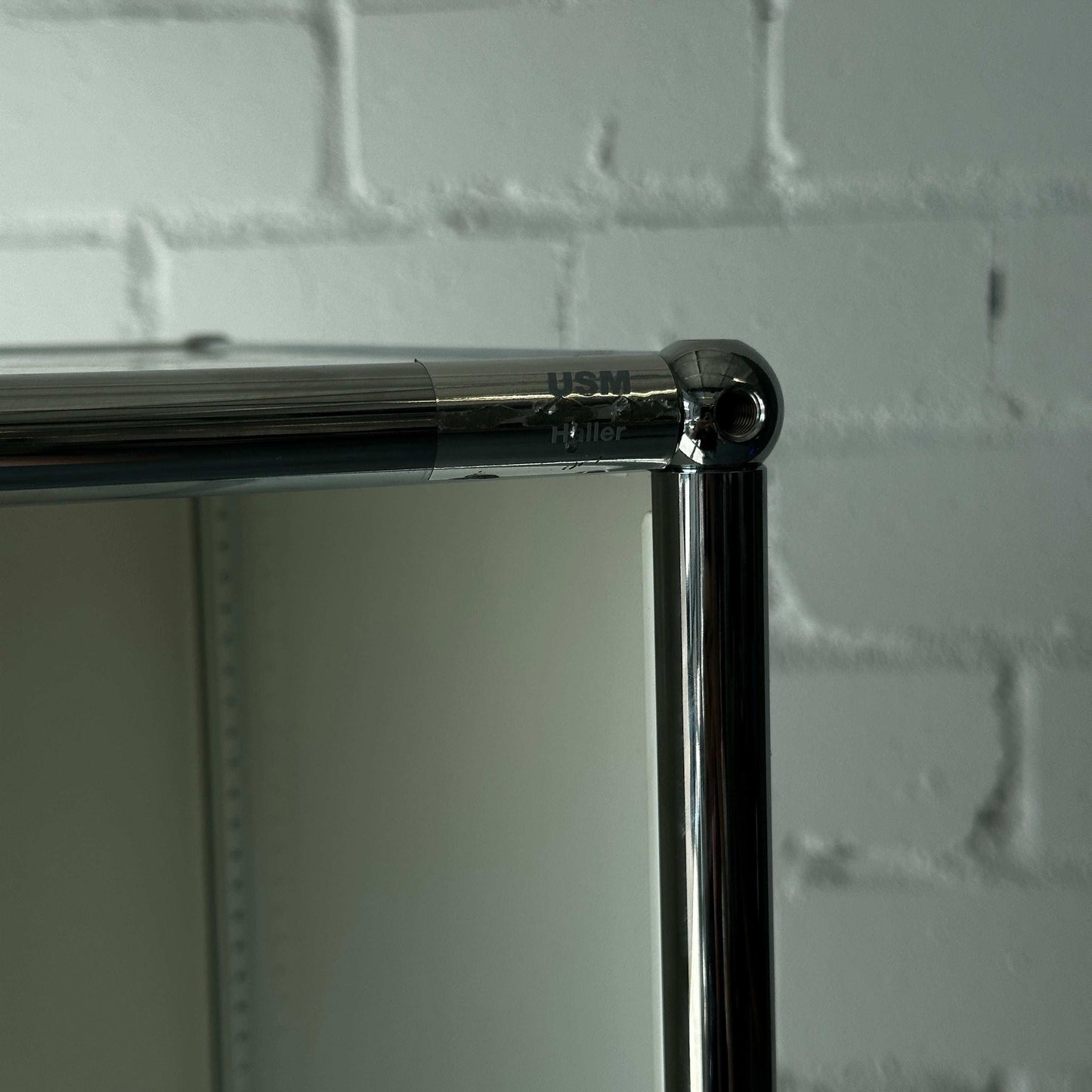 USM Haller 1x6 Highboard weiß mit drei Klappen und verchromtem Rahmen vor weißer Ziegelwand