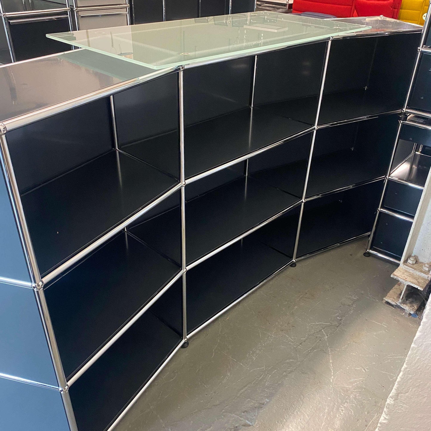 USM Haller anthracite reception desk with glass top and modular shelving units in curved design