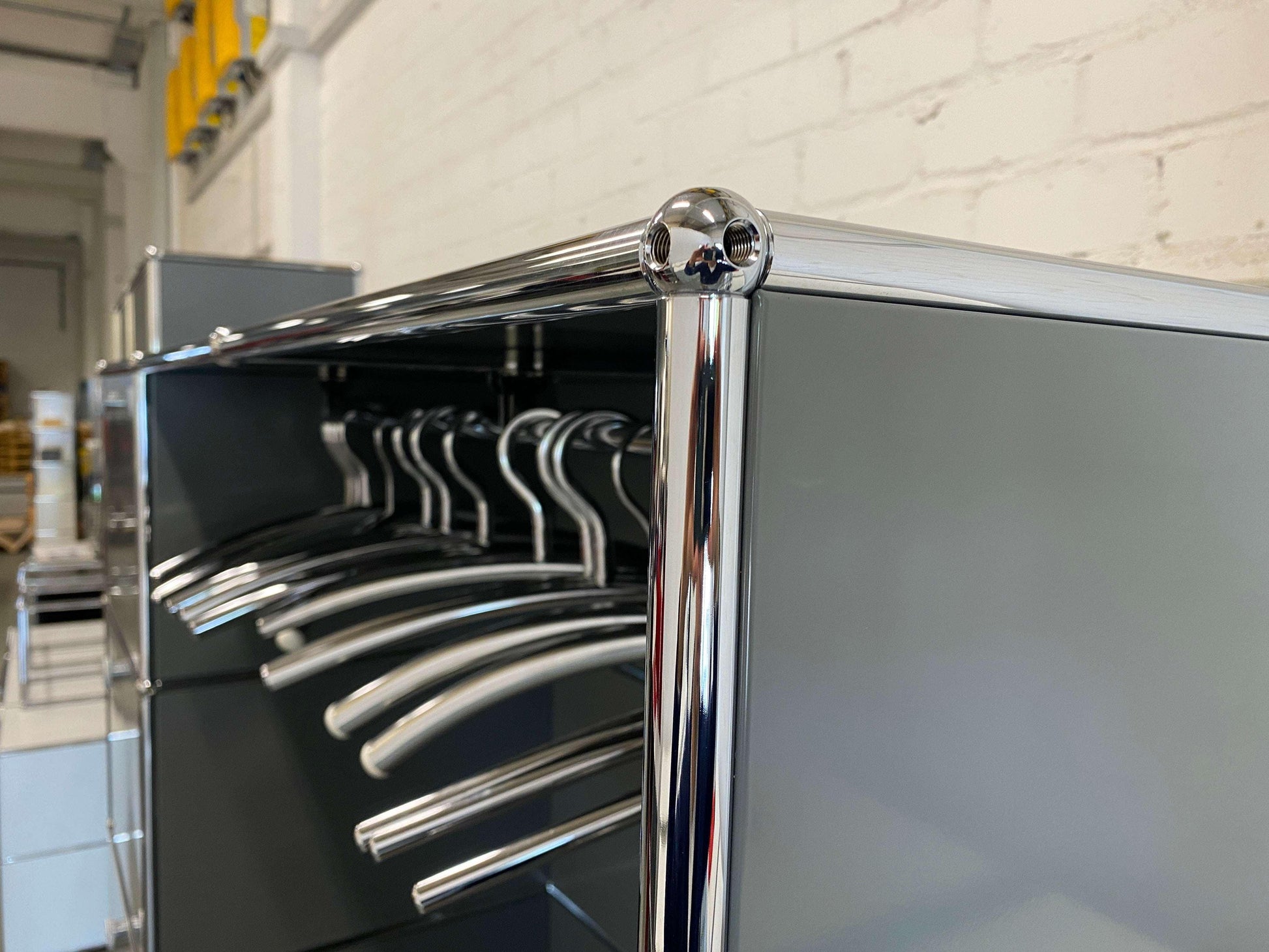 Close-up of USM Haller Garderobe with chrome frame and grey panels showing hanging metal clothes hangers.