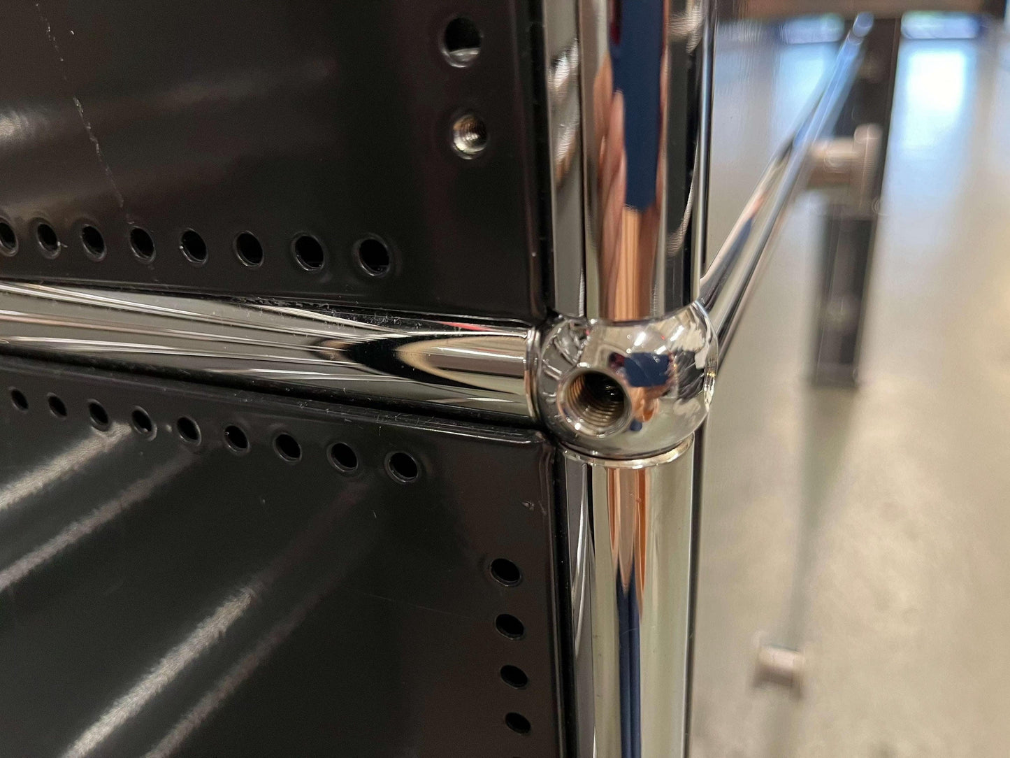 Close-up of black USM Haller Highboard corner with chrome metal connectors and perforated steel panels.