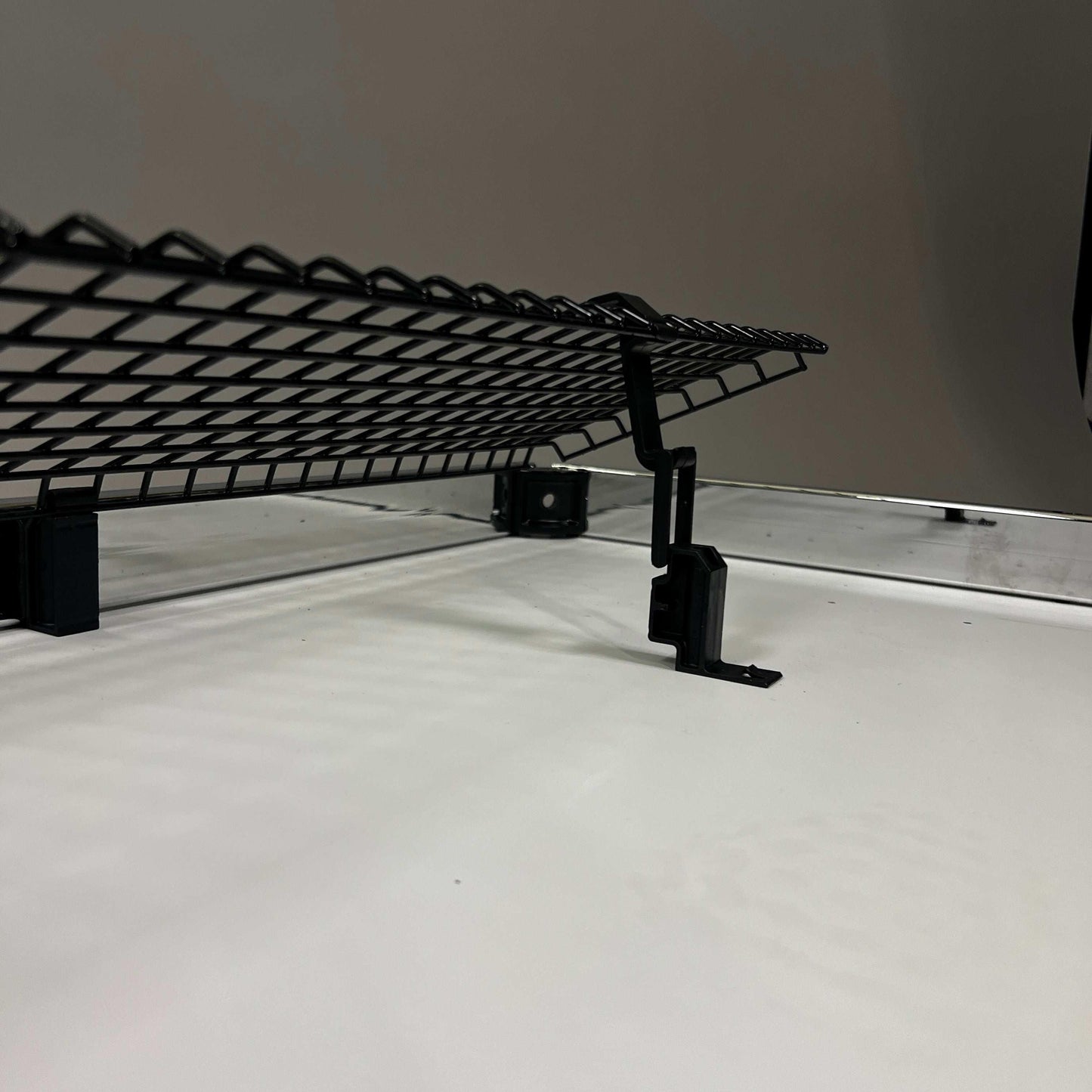 Black foldable USM Haller cable basket mounted under a desk for cable management with included fastening accessories