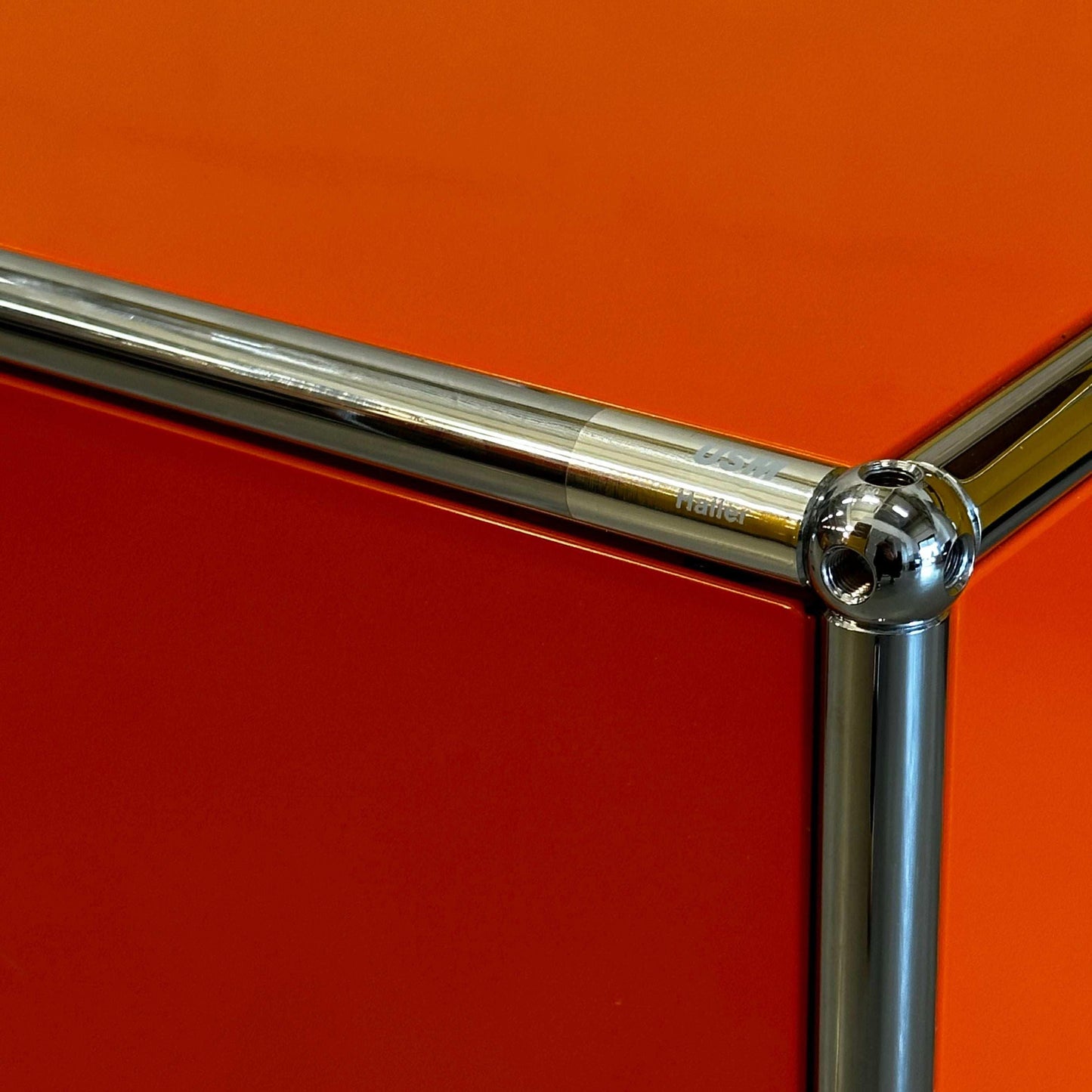 Close-up of USM Haller Lowboard corner in reinorange with chrome metal frame.
