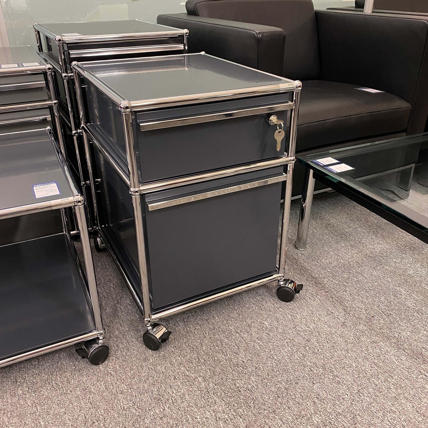 USM Haller anthracite roll container with two drawers on casters next to a sofa and glass table