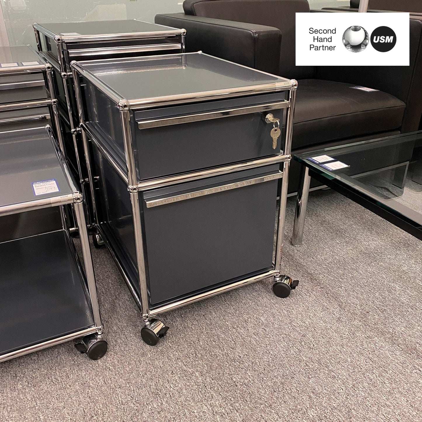 USM Haller anthracite roll container with two drawers on casters next to a sofa and glass table