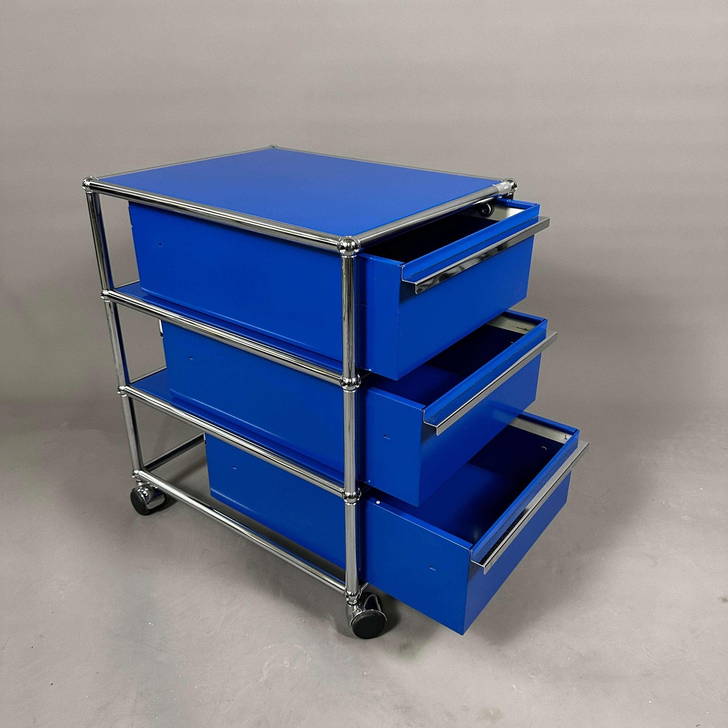 USM Haller Rollcontainer enzianblau mit drei geöffneten Schubladen auf Rollen