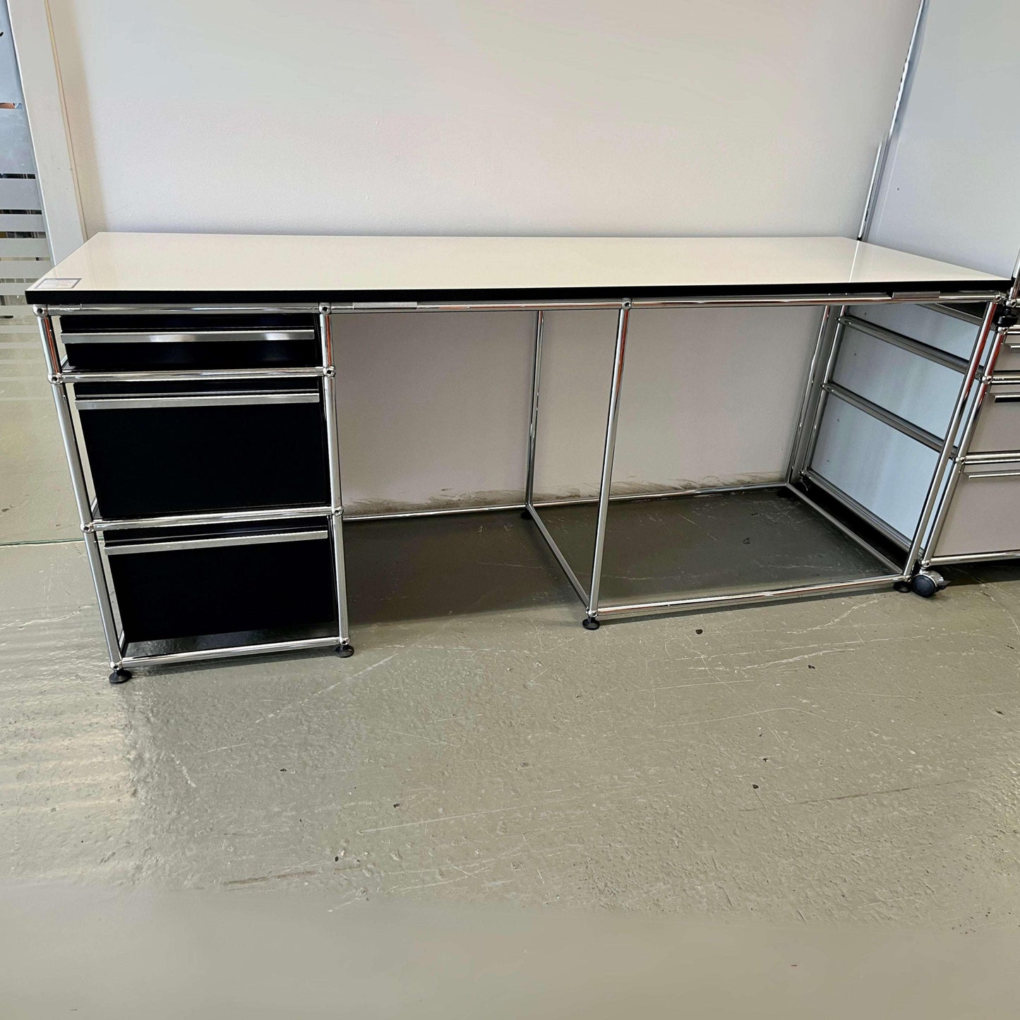 USM Haller office desk with pearl gray tabletop, black edge, and graphite black drawer unit, metal frame.