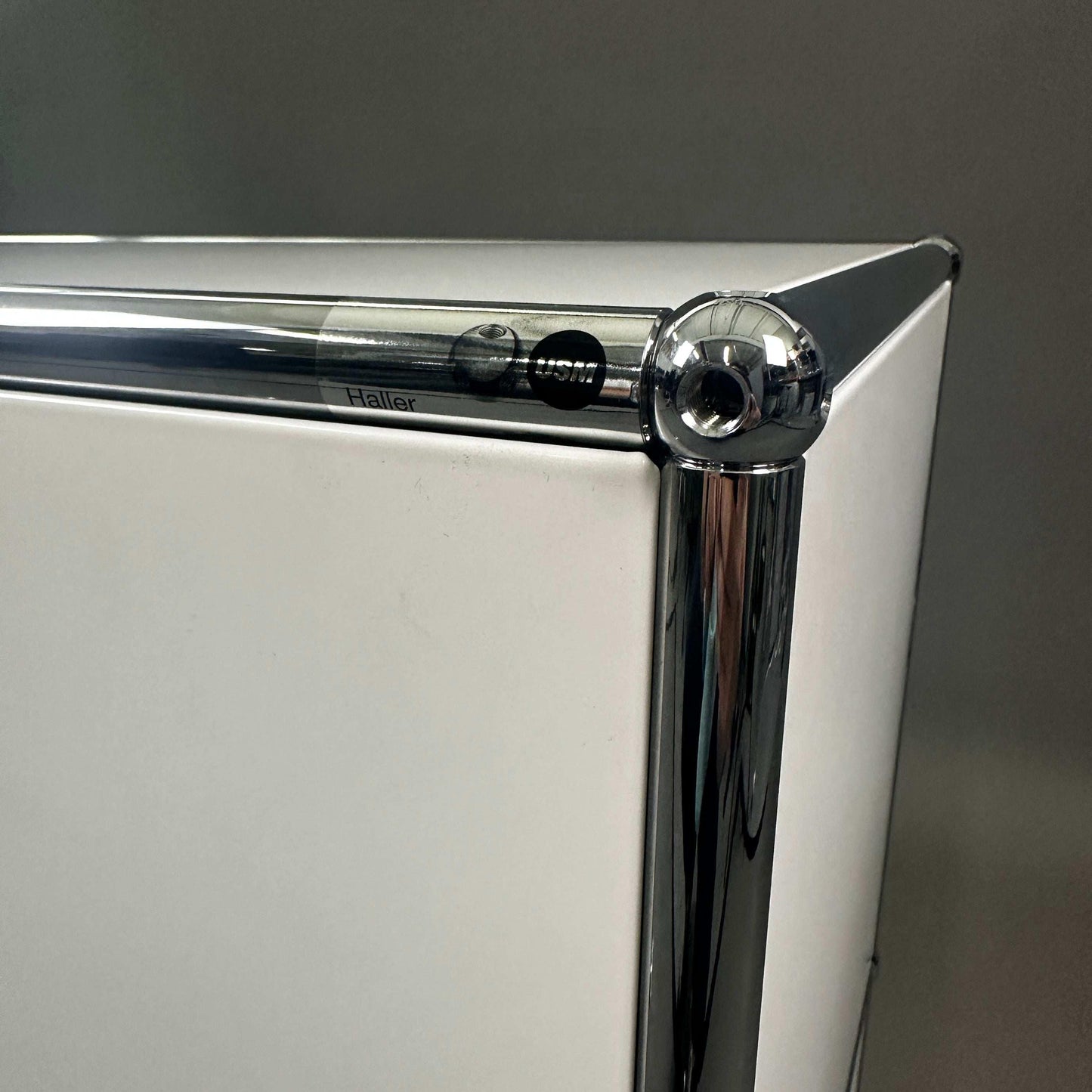 Close-up of white USM Haller sideboard corner with chrome metal frame and 2 flap compartments