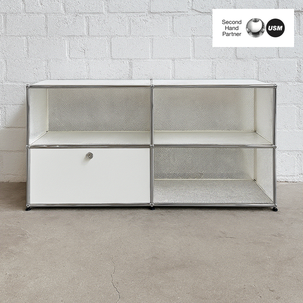 USM Haller Sideboard 2x2 weiß mit einer abschließbaren Klappe und perforierten Tablare vor weißer Ziegelwand