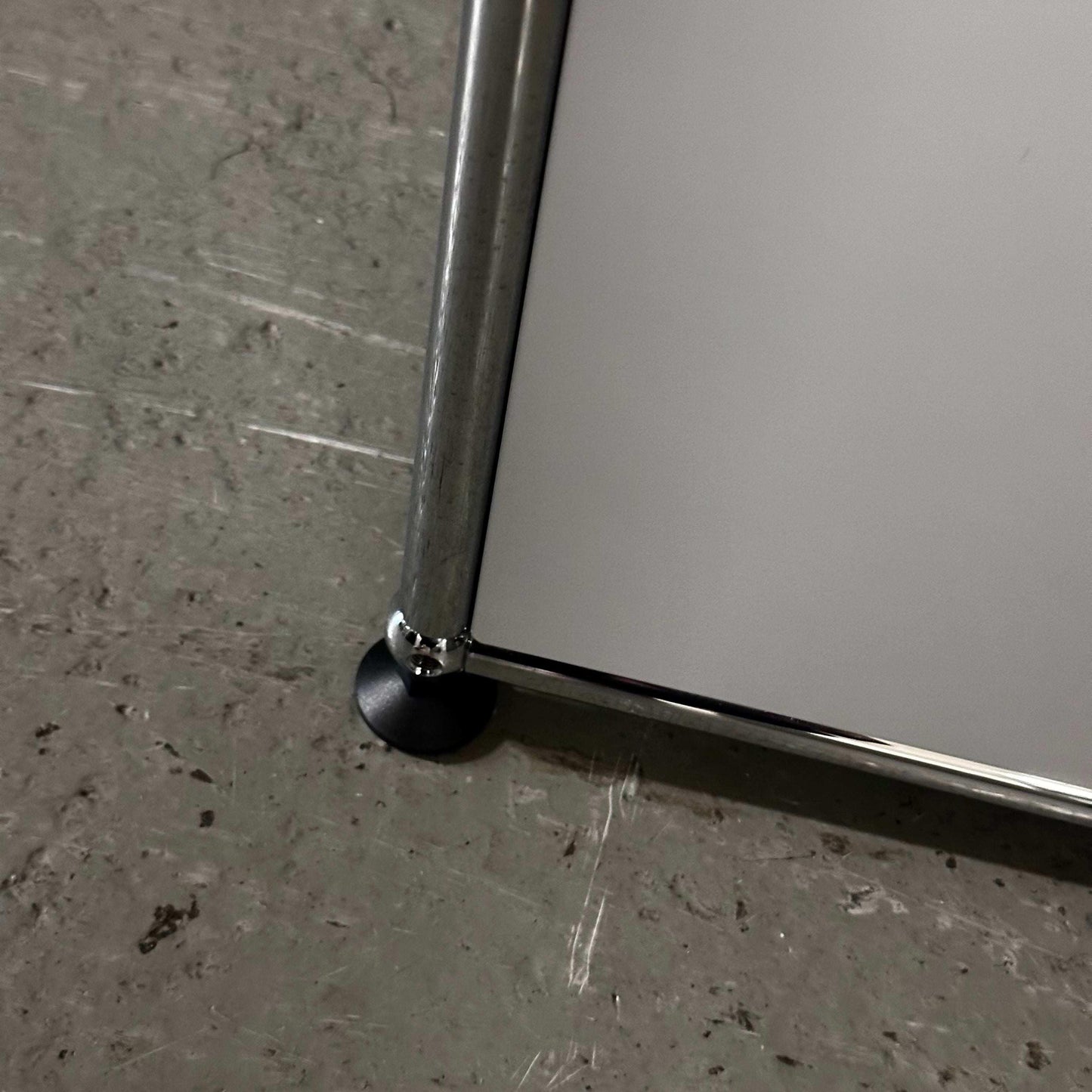 Close-up of the light gray USM Haller Sideboard corner with chrome leg on concrete floor