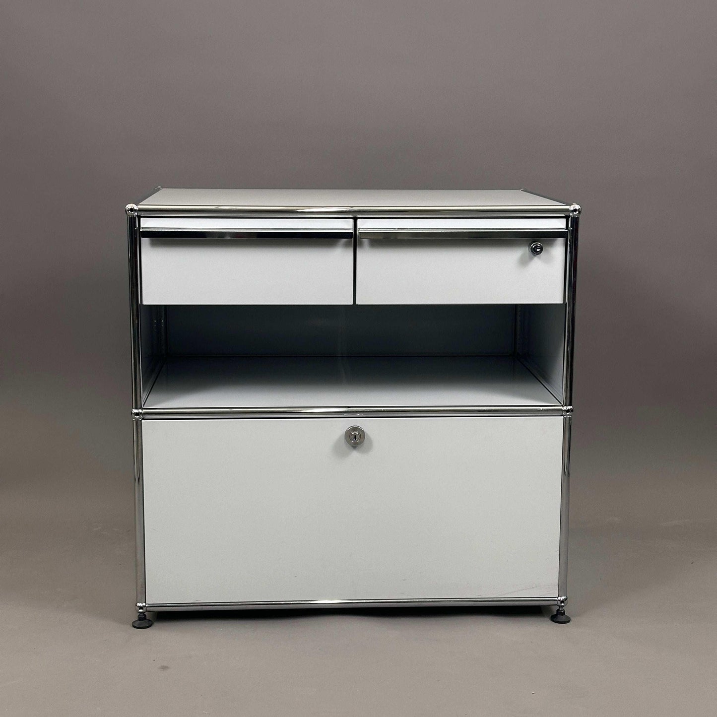 USM Haller Sideboard lichtgrau mit zwei Schubladen und abschließbarem Auszug auf grauem Hintergrund