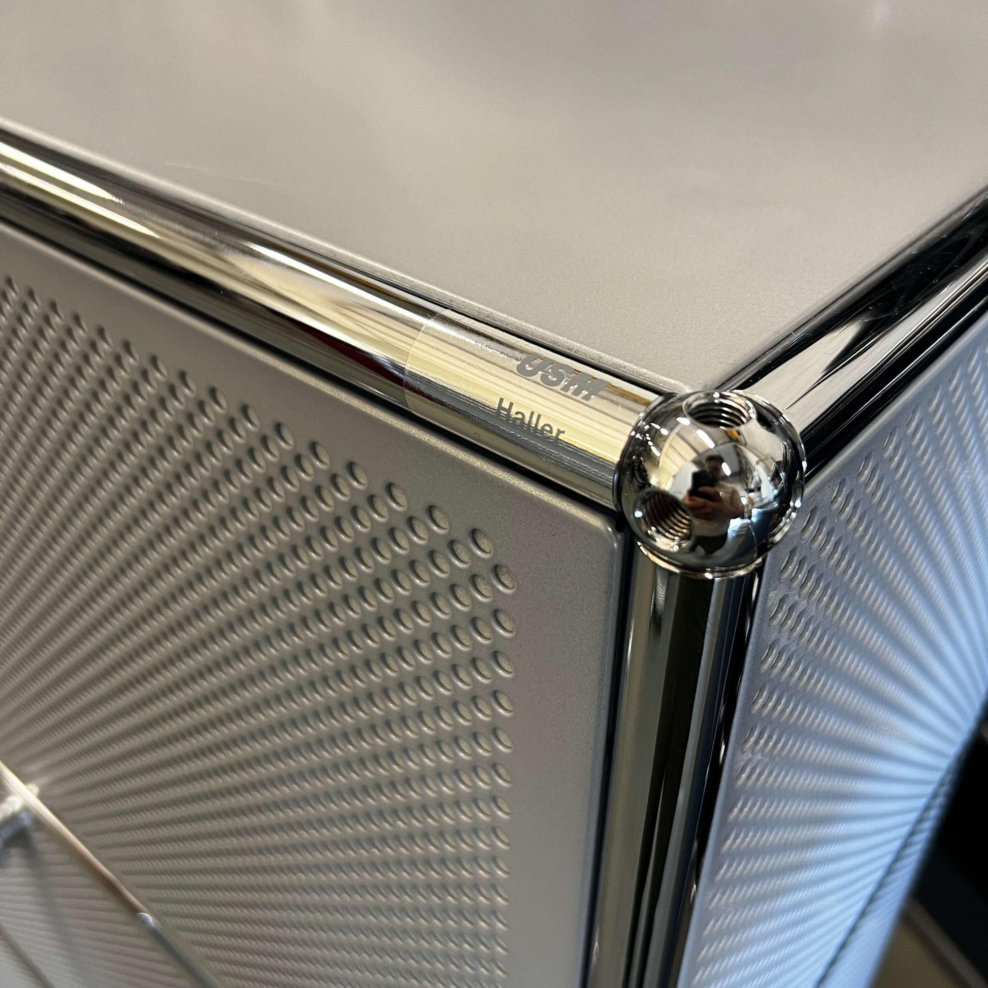 Close-up of USM Haller Sideboard in matte silver with perforated sound-absorbing panels and chrome frame detail