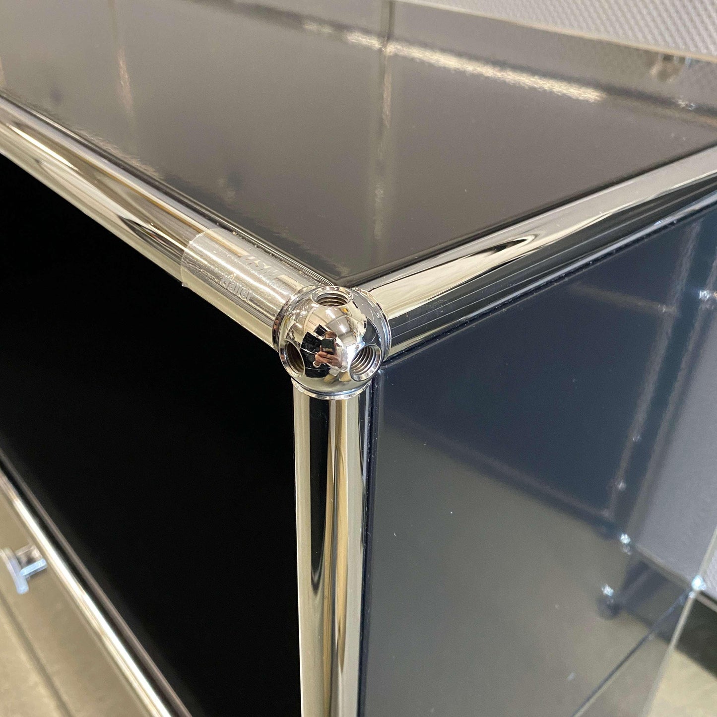 Close-up of black USM Haller Sideboard corner with chrome tubing and glossy surface, featuring three flap doors