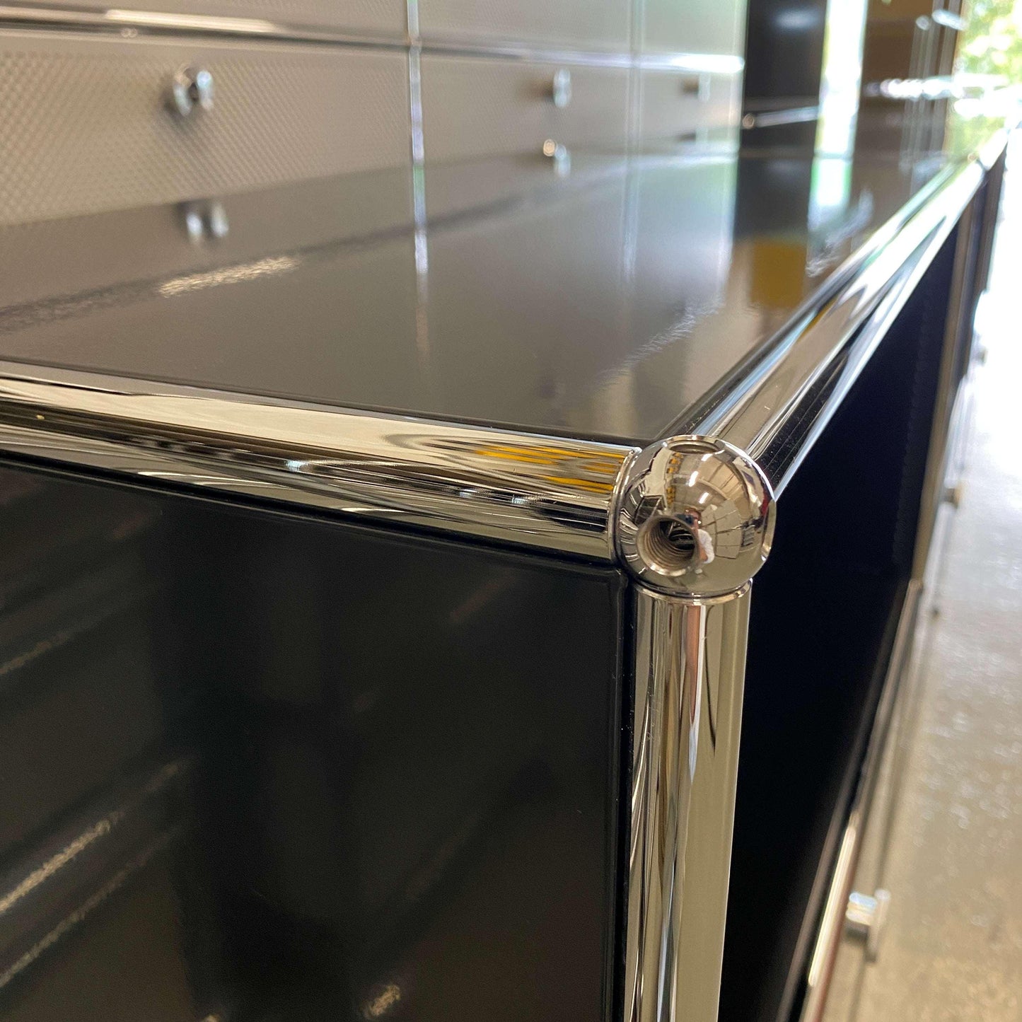 Close-up of black USM Haller Sideboard with three flap doors and chrome frame detailing