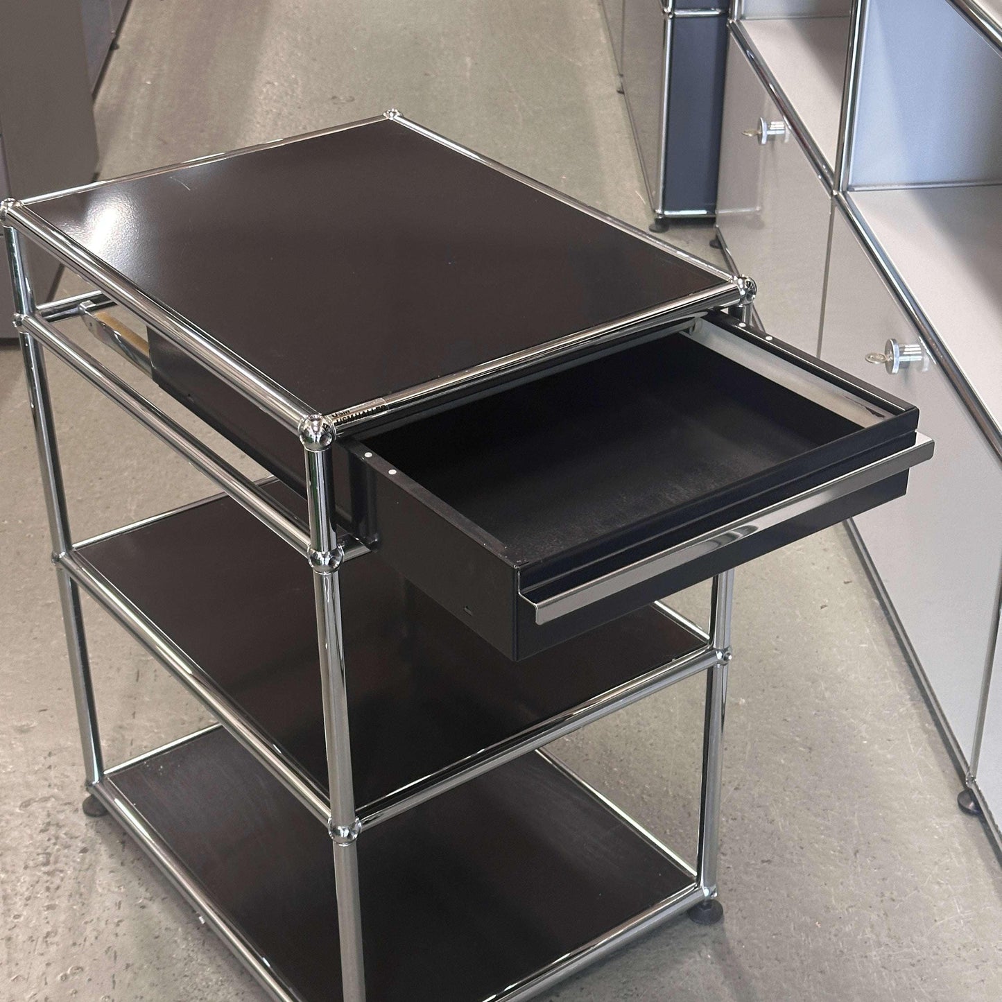 USM Haller Standcontainer Nachttisch graphitschwarz mit einer offenen Schublade und drei Ablageflächen