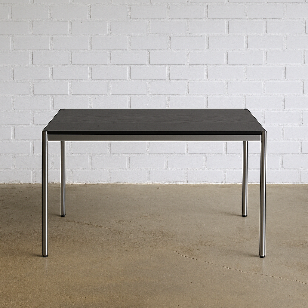 USM Haller Tisch 125x75cm mit schwarzer Eichenplatte und Chromgestell vor weißer Ziegelwand
