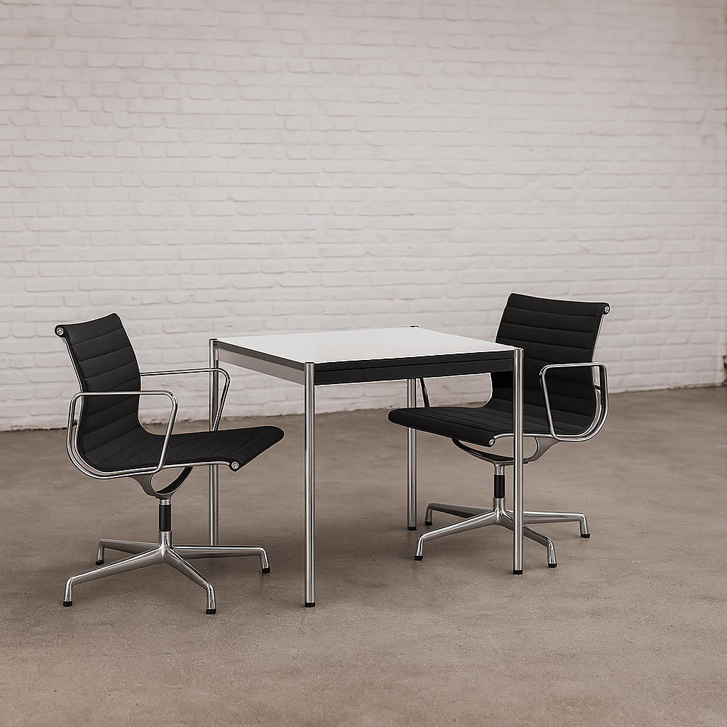 USM Haller Tisch 75x75 cm in perlgrau und weiß mit chromgestell, minimalistischer Arbeitstisch mit zwei schwarzen Bürostühlen vor weißer Ziegelwand