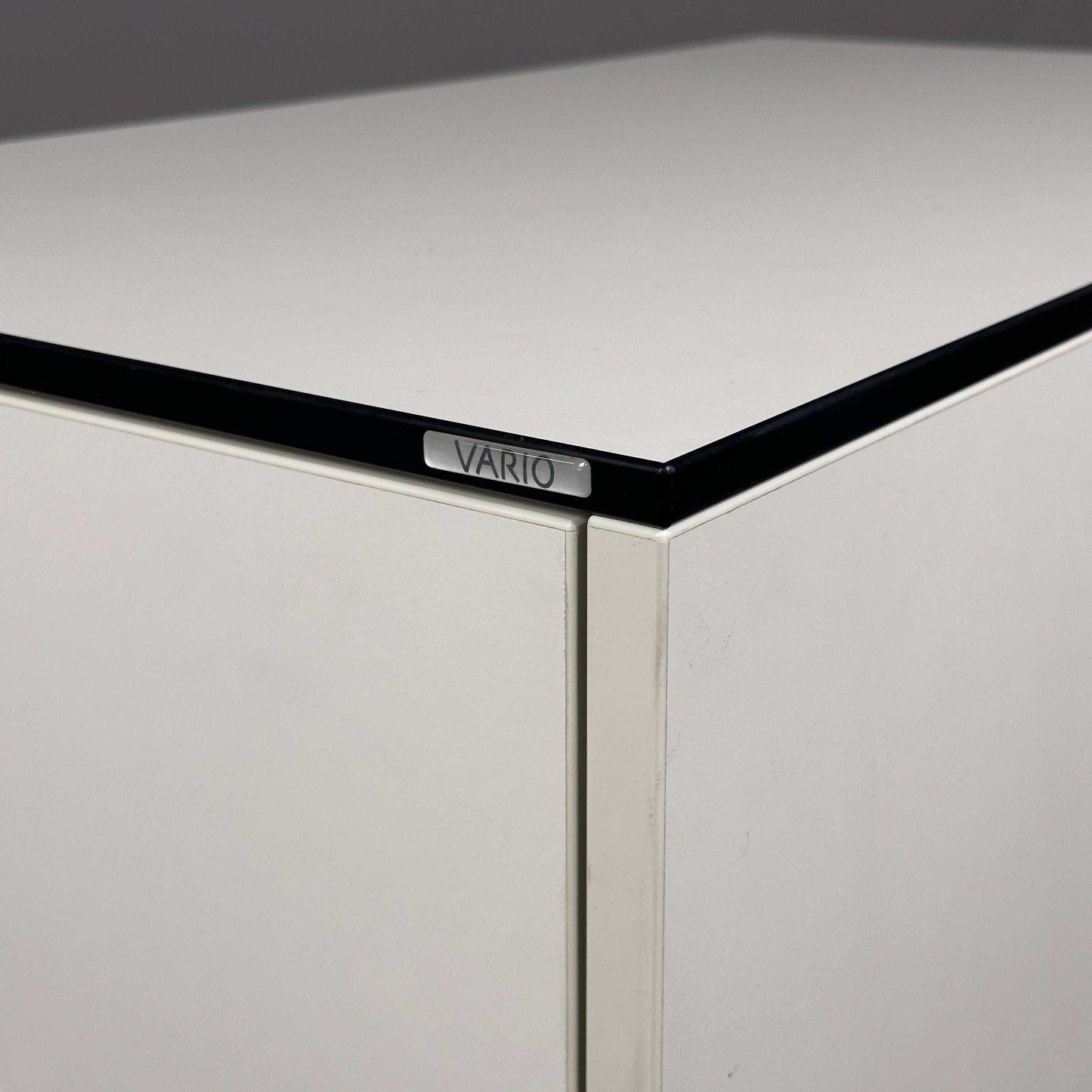weißer Vario Apothekerschrank mit schwarzer Kante und Vario-Logo nahaufnahme Ecke