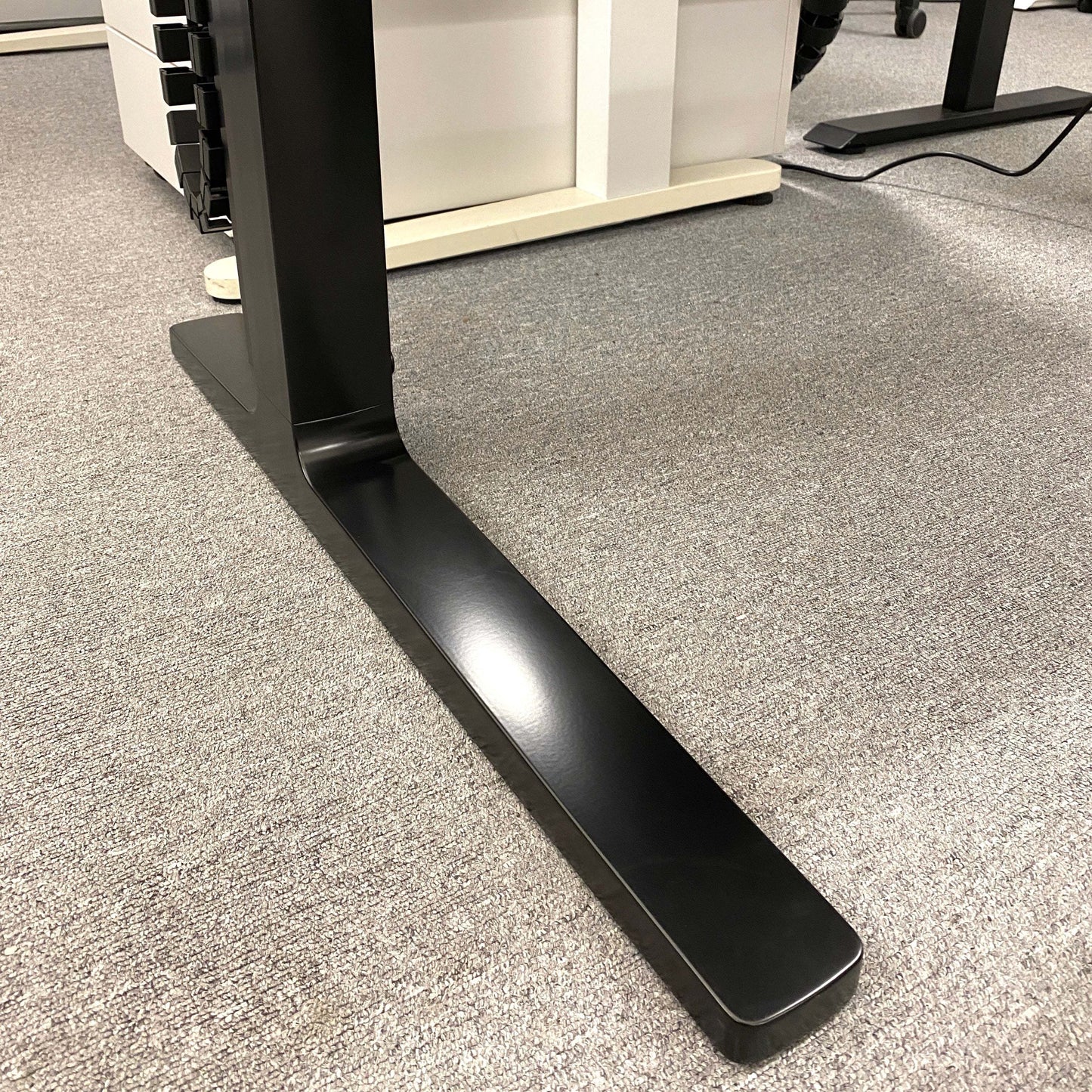 Close-up of black C-foot frame of Vario Change 180x80cm electric height adjustable desk on grey carpet