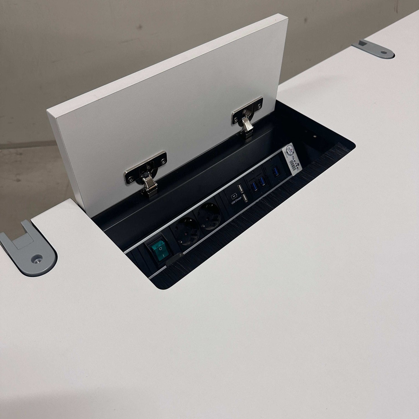 Vario Stage Schreibtisch mit weißer Platte, chromfarbener Gestell, integrierter Kabelführung und Bachmann Steckdosenleiste mit USB-Anschlüssen.