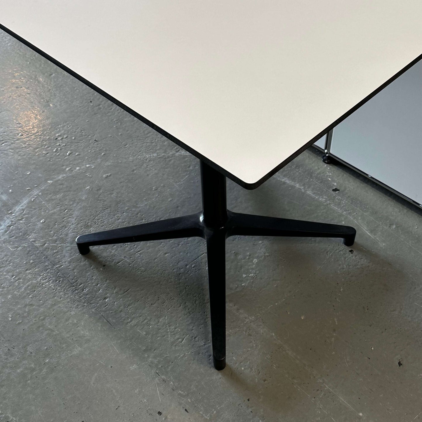 Vitra Bistro Table with white rectangular top and black metal pedestal base on concrete floor