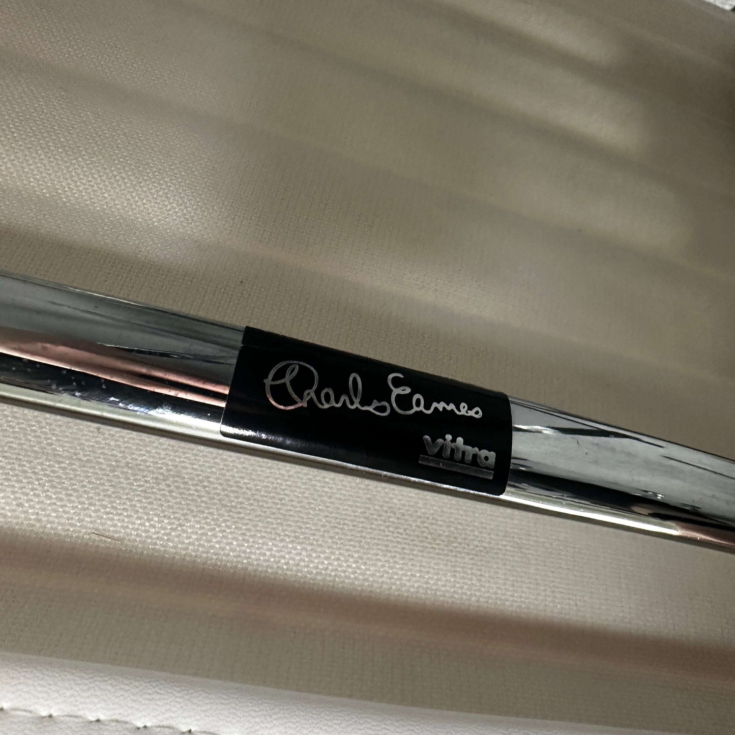 Close-up of Vitra EA 101 chair chrome frame with Charles Eames signature badge on white leather upholstery