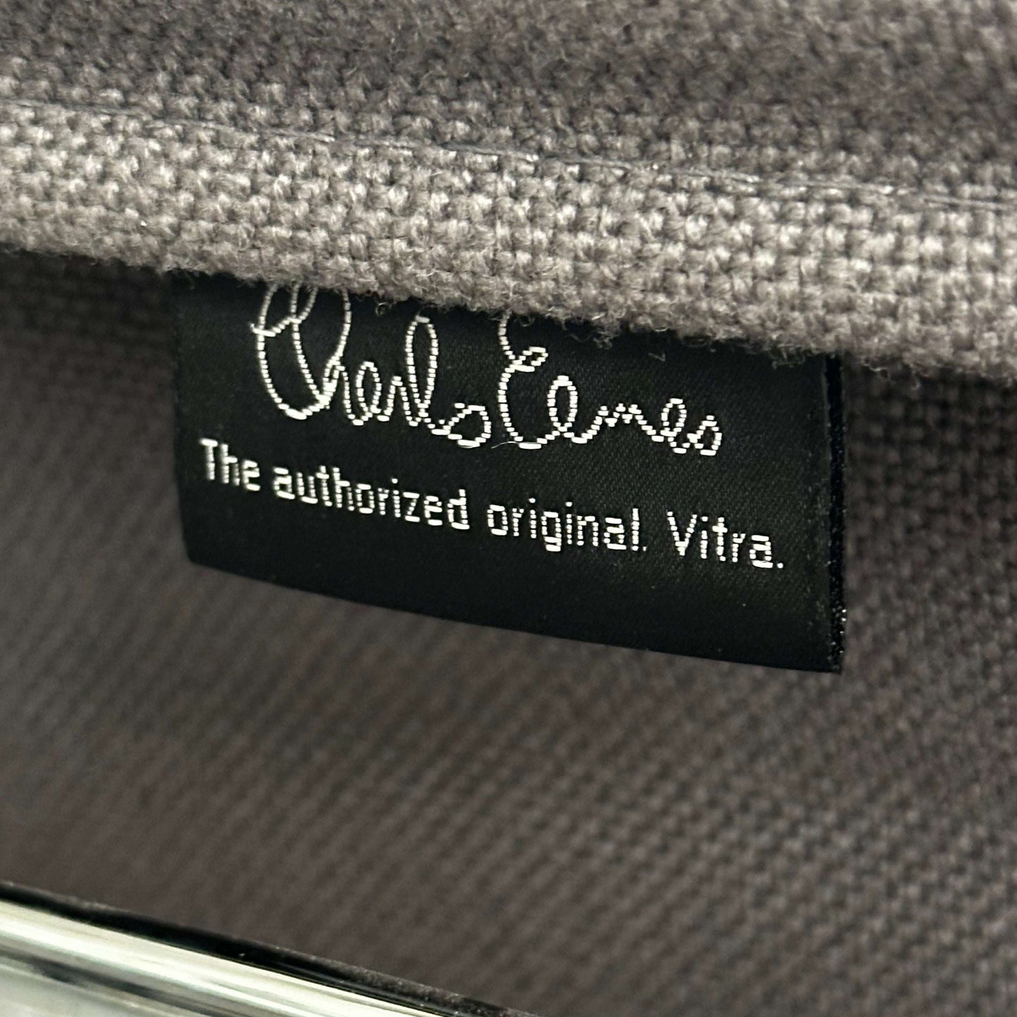 Close-up of a Vitra EA 107 chair label on medium grey hopsak fabric, non-swivel model